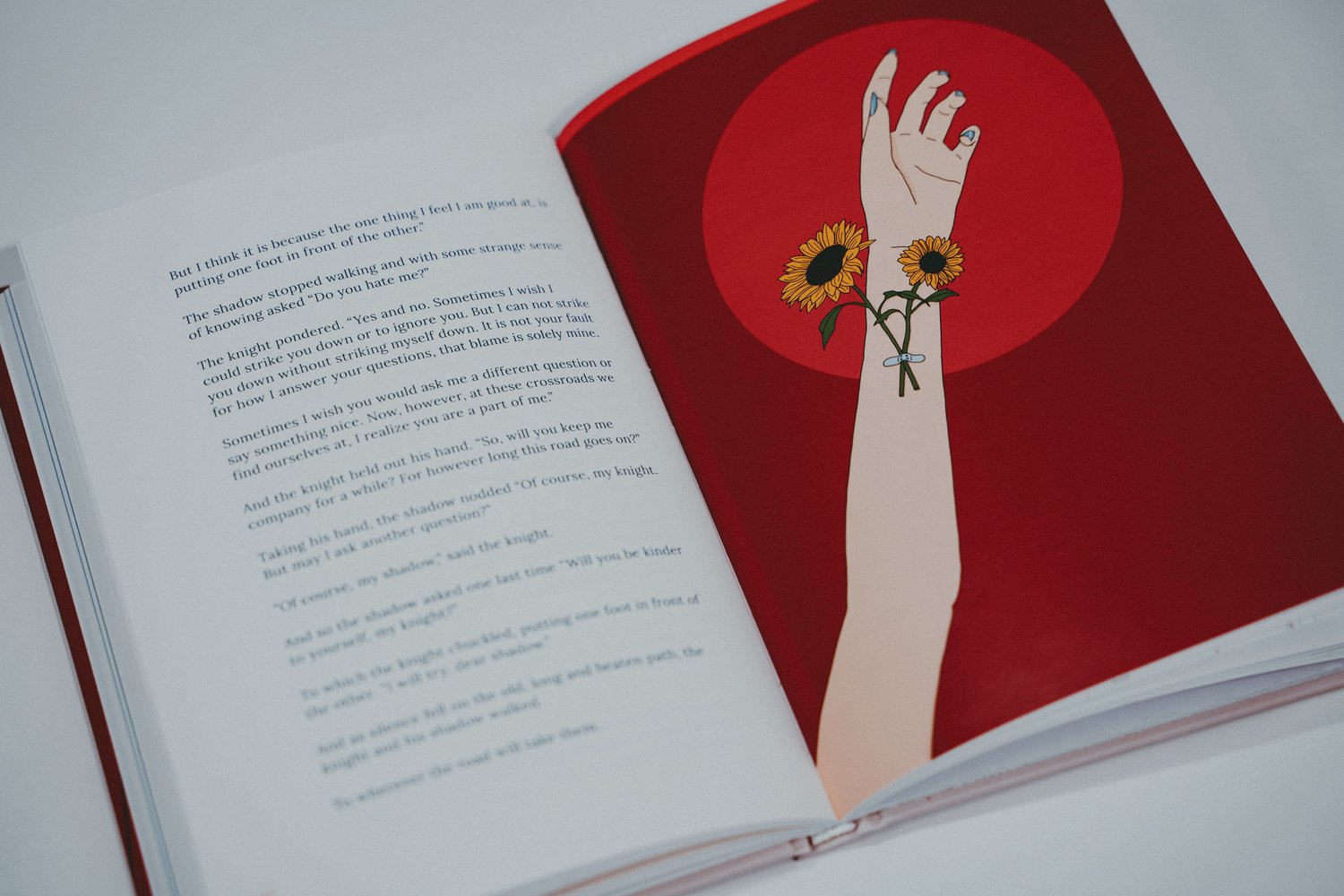 Open boek op een lichte ondergrond. Op de linkerpagina staat Engelstalige tekst. Op de rechterpagina staat een illustratie van een arm met een pleister en twee zonnebloemen tegen een rode achtergrond.