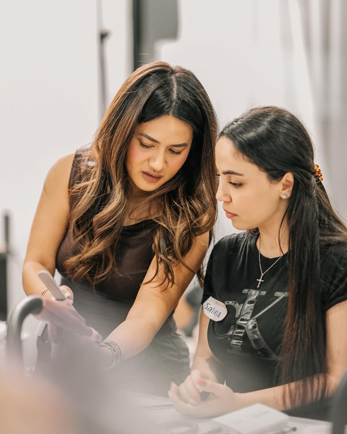 Nail technician reviewing nail polish and gel bottles in a modern studio, selecting high-quality products for professional nail services.