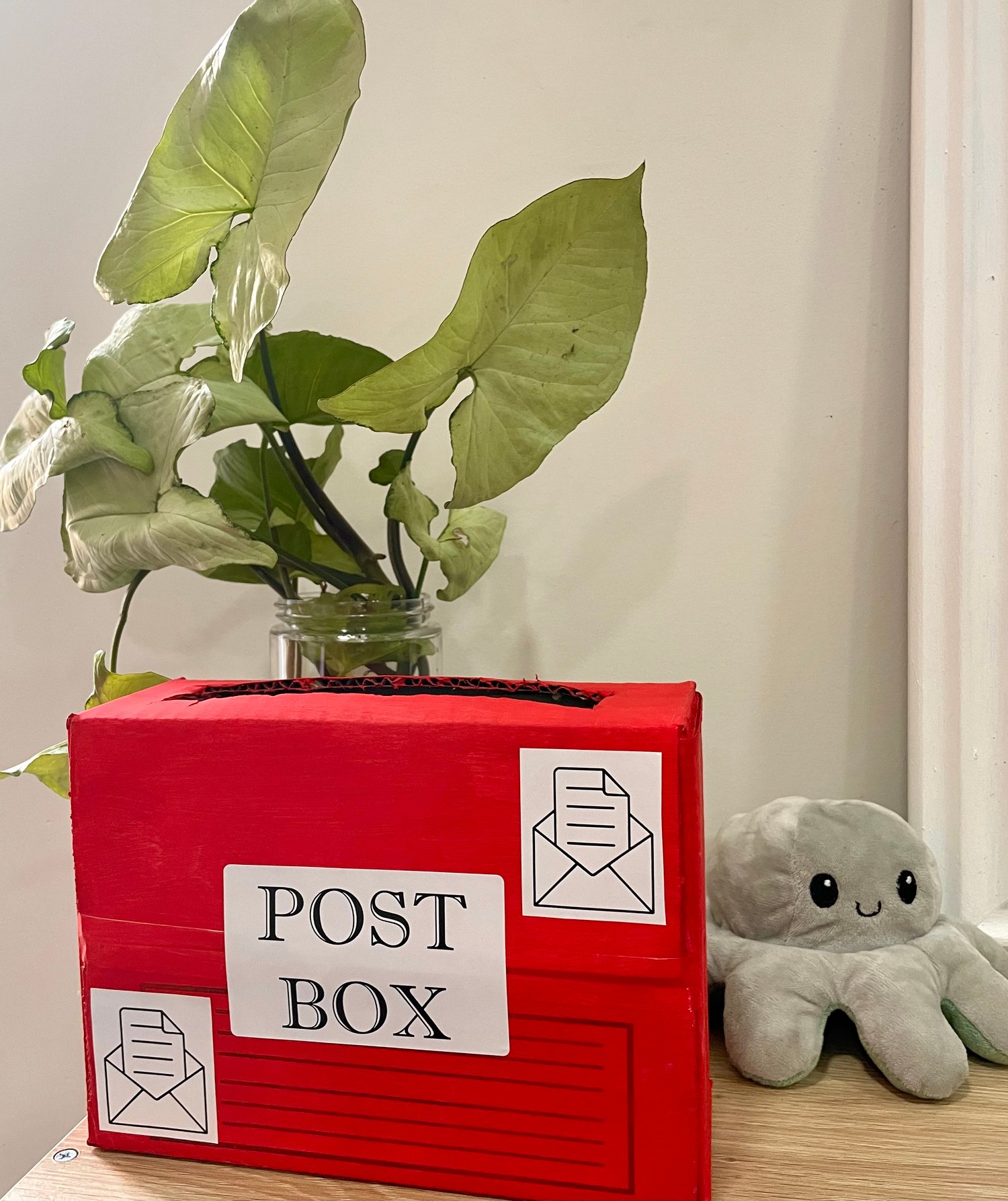 red handmade postbox with a decorative leafy water plant in the background and a smiling toy octopus