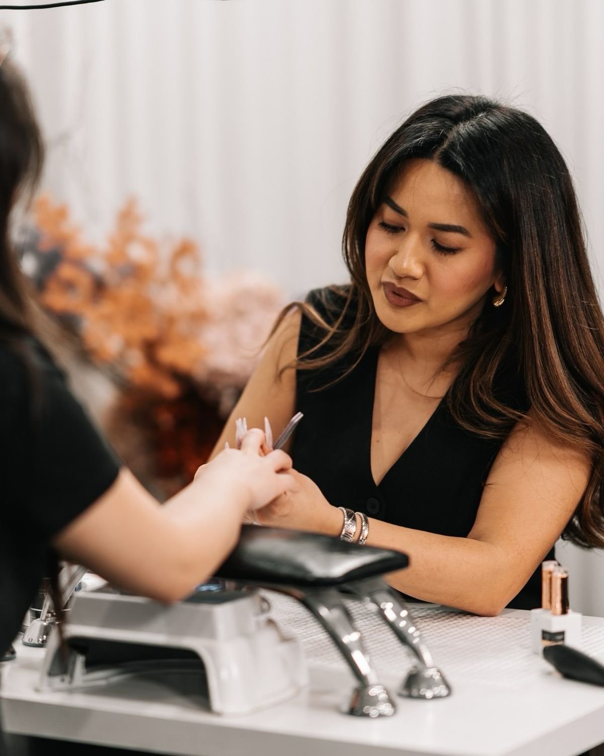 Nail technician managing client appointments on a laptop and smartphone in a clean studio, demonstrating an efficient booking system for nail techs.