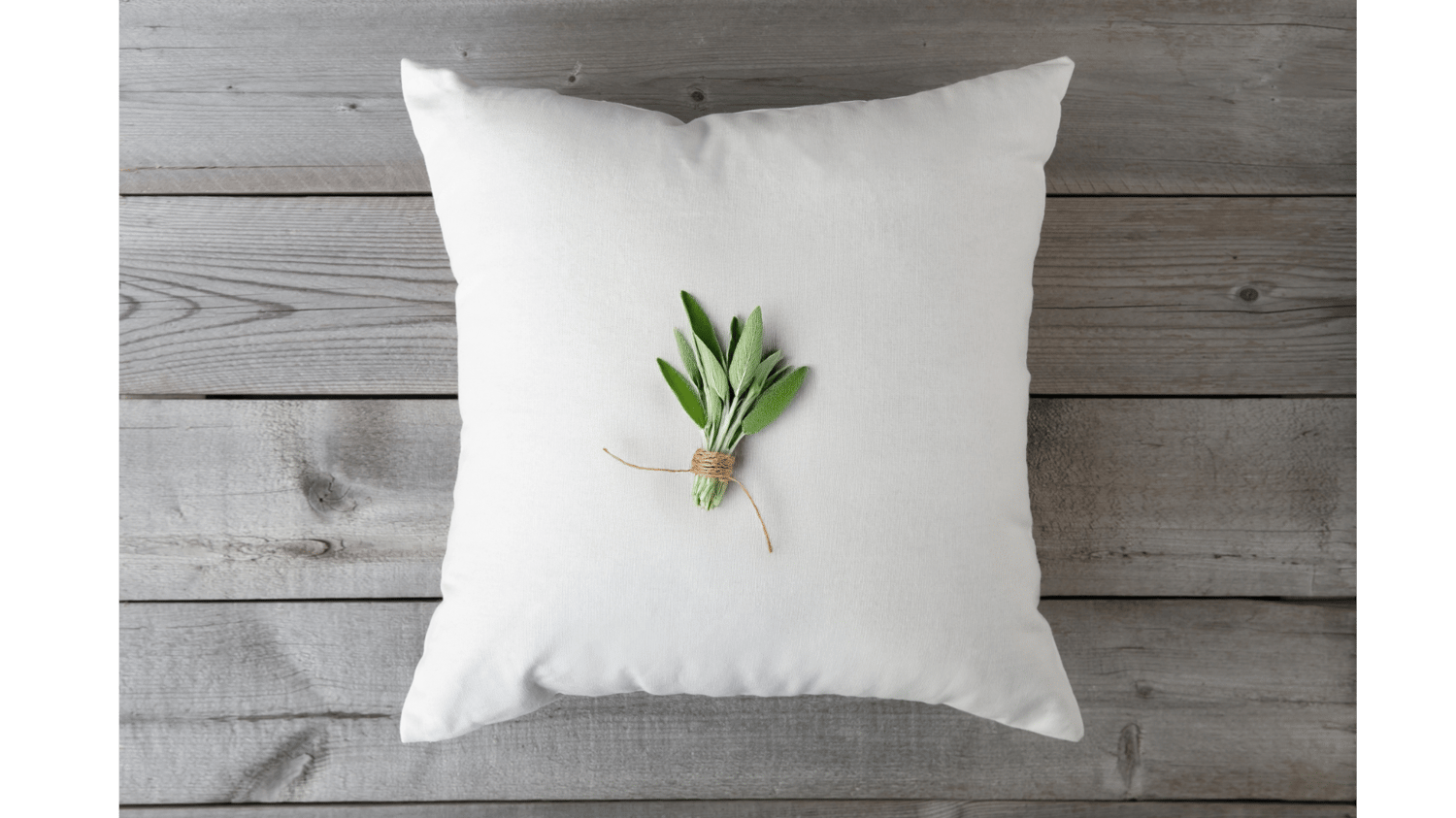 pillow on a wood background with a bundle of sage on top