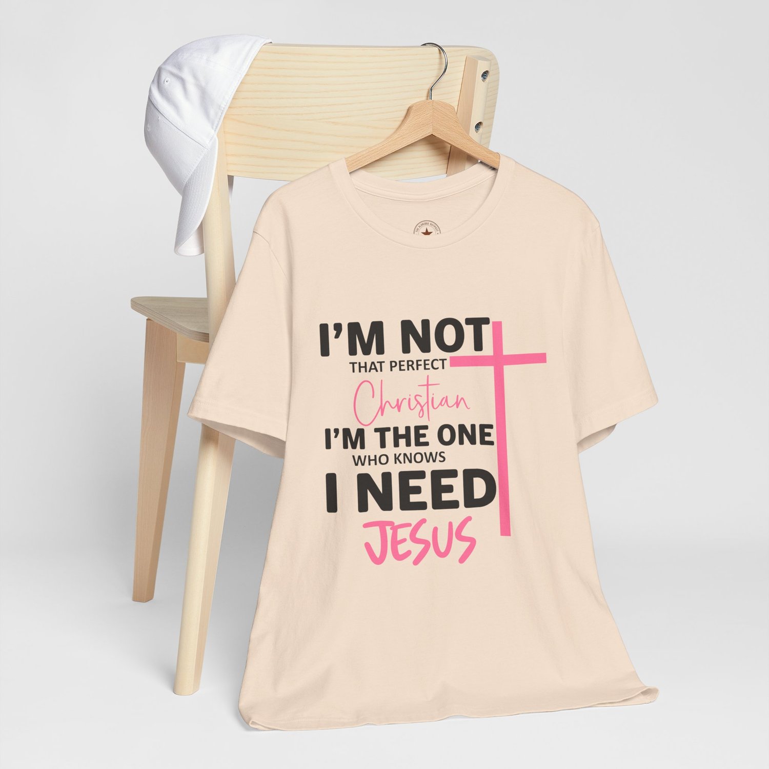 Outpost Standard sand-colored t-shirt with Spring Pink Need Jesus design and vertical cross graphic.