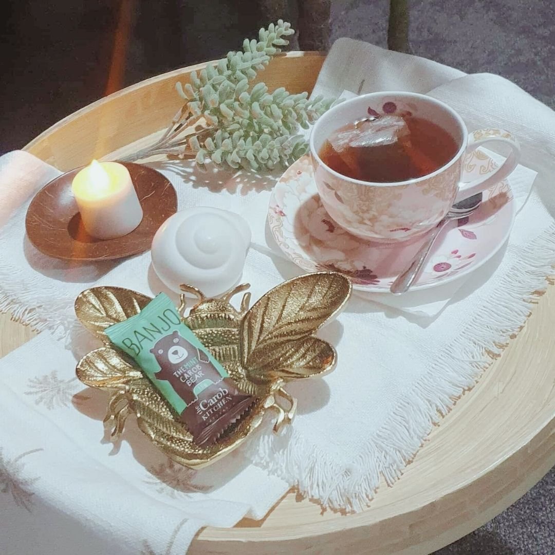 Cosy wellness styled flat lay of herbal tea, burning candle and carob chocolate bear representing the natural health and self care philosophy at Inner Bliss Wellness Space Oxenford Area