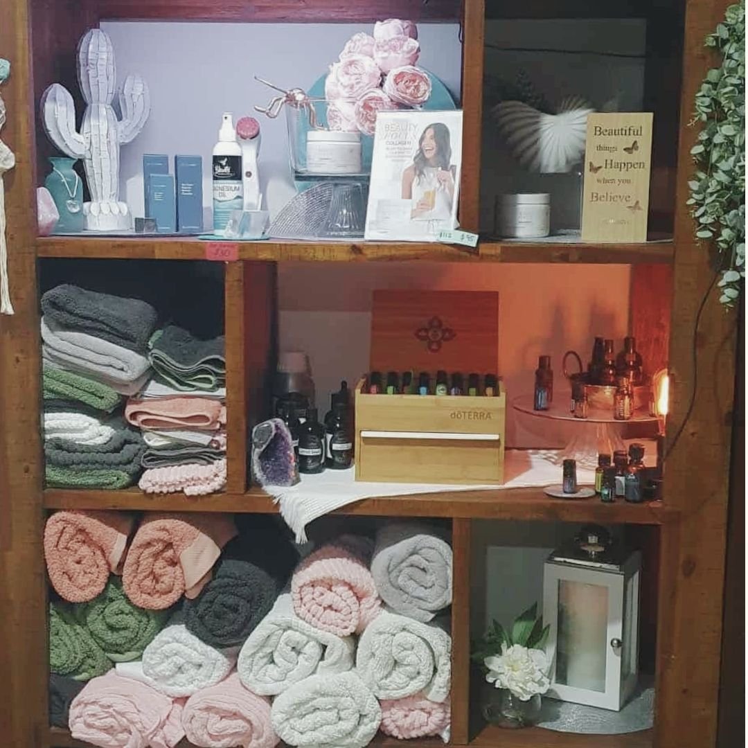 Natural wellness product shelf styled with essential oils, towels and holistic health products representing the nurturing treatment environment at Inner Bliss Wellness Space Upper Coomera Area
