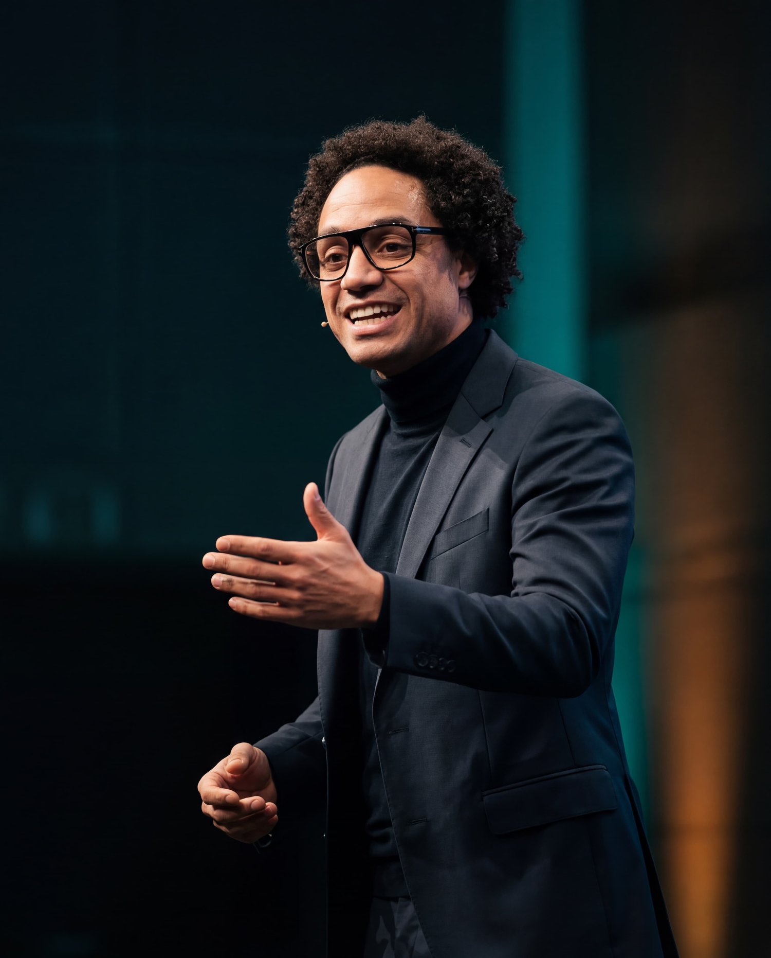 Benjamin AZIKA-EROS, Expert en Ingénierie de la Performance, capturé dans une pose de conférence dynamique et autoritaire. Éclairage industriel teal et ambre soulignant l'expertise technique et la maîtrise systémique.