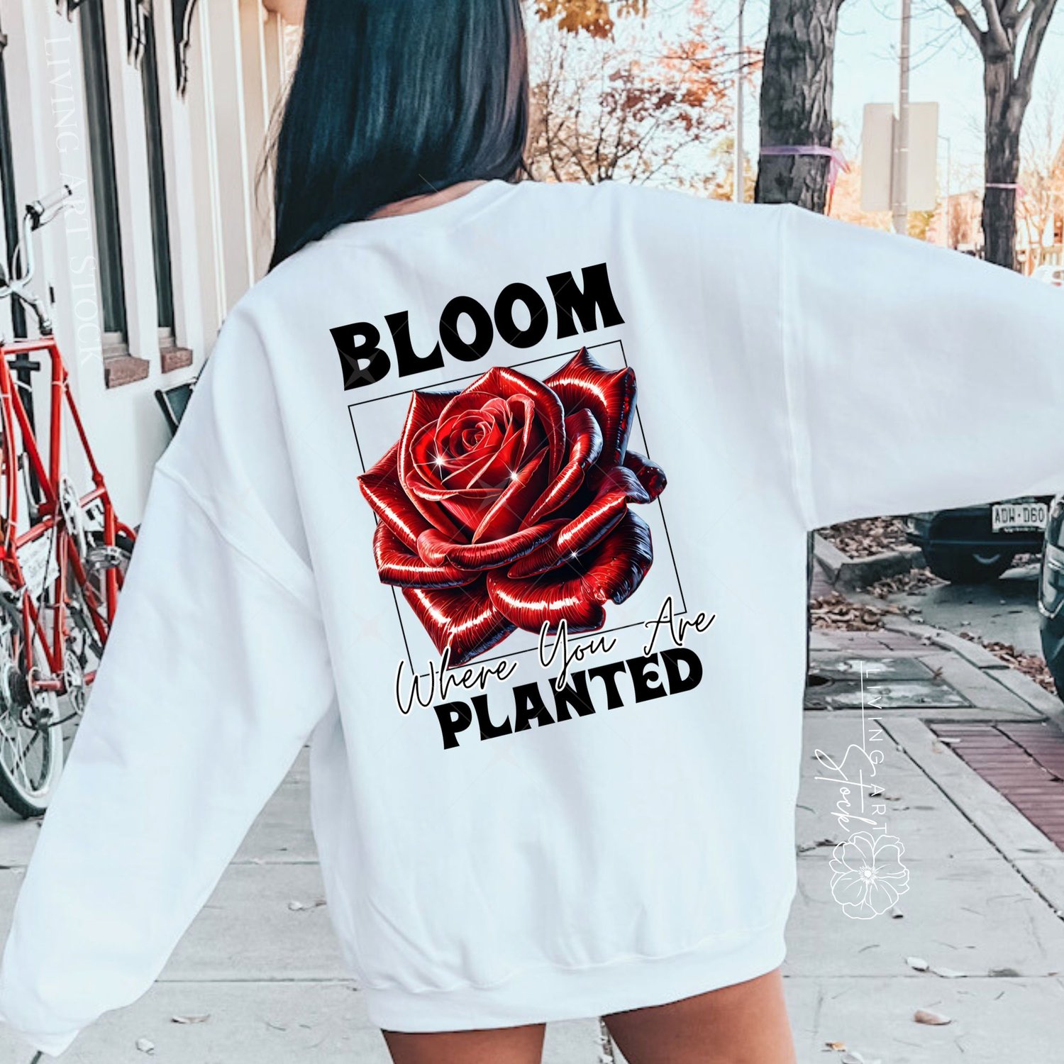 A vibrant t-shirt graphic design featuring a hyper-realistic, glossy red rose with a metallic sheen, set within a black wireframe square. Bold, chunky text above reads "BLOOM", and text below in script and bold fonts reads "Where You Are planted", all on 