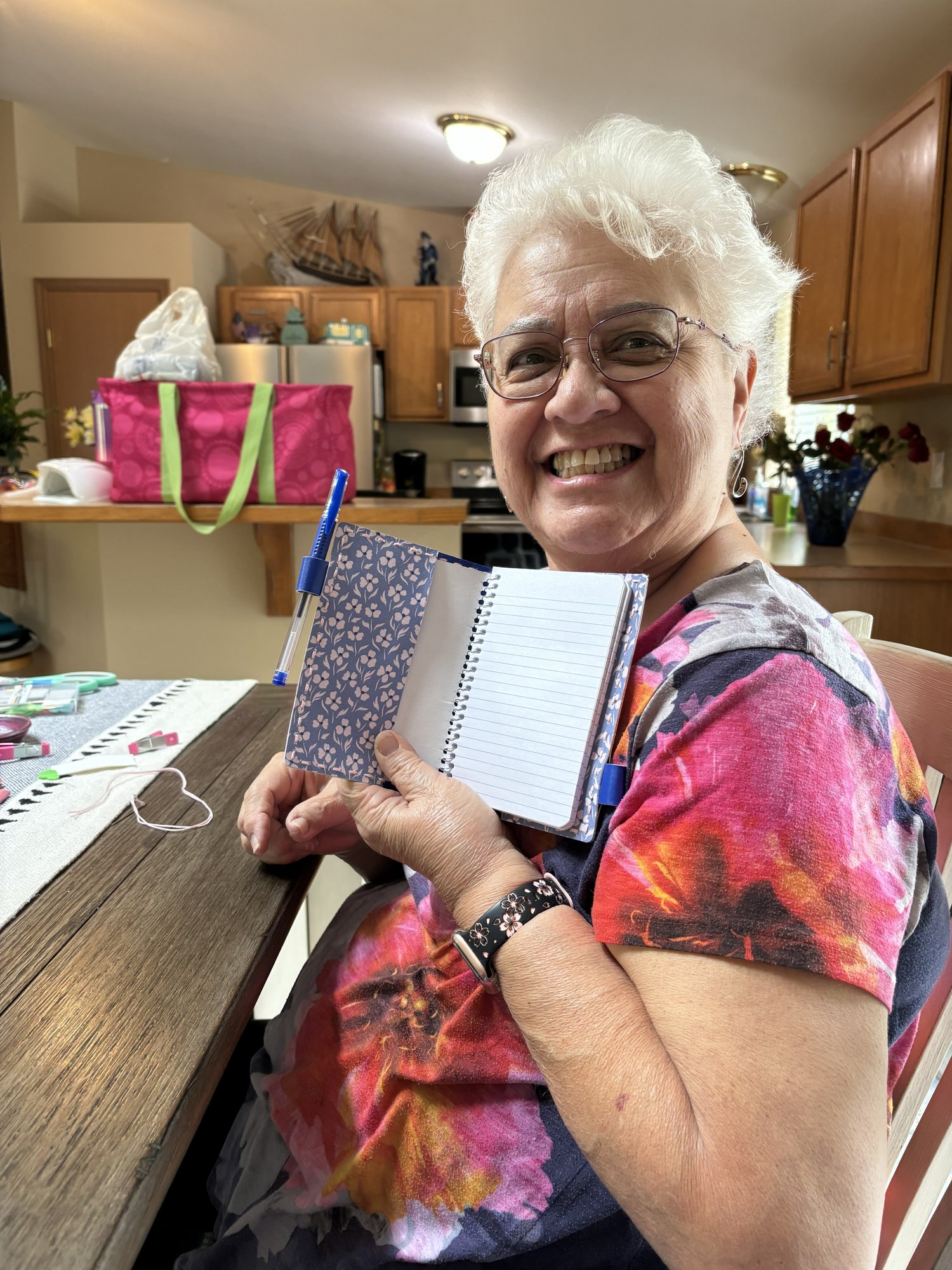 Participant seated at a table, smiling while holding up their finished easy stitch notebook with a patterned cover.