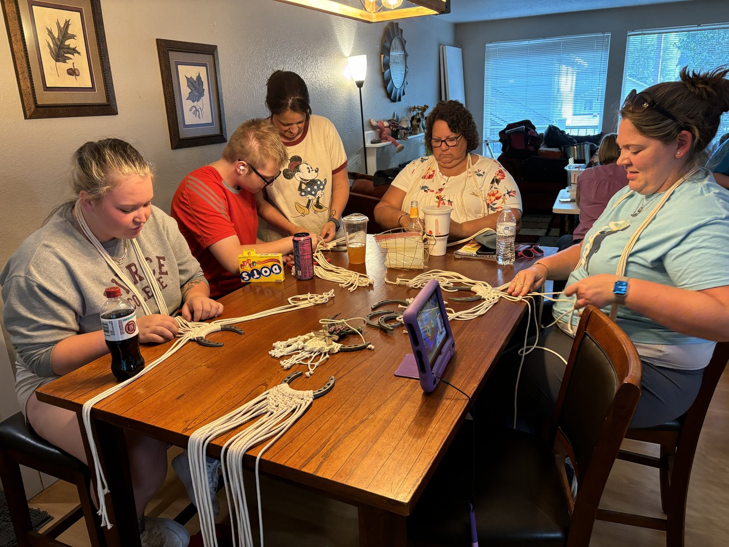 Participants gathered around a table creating horseshoe macramé projects with yarn and supplies spread out in front of them.