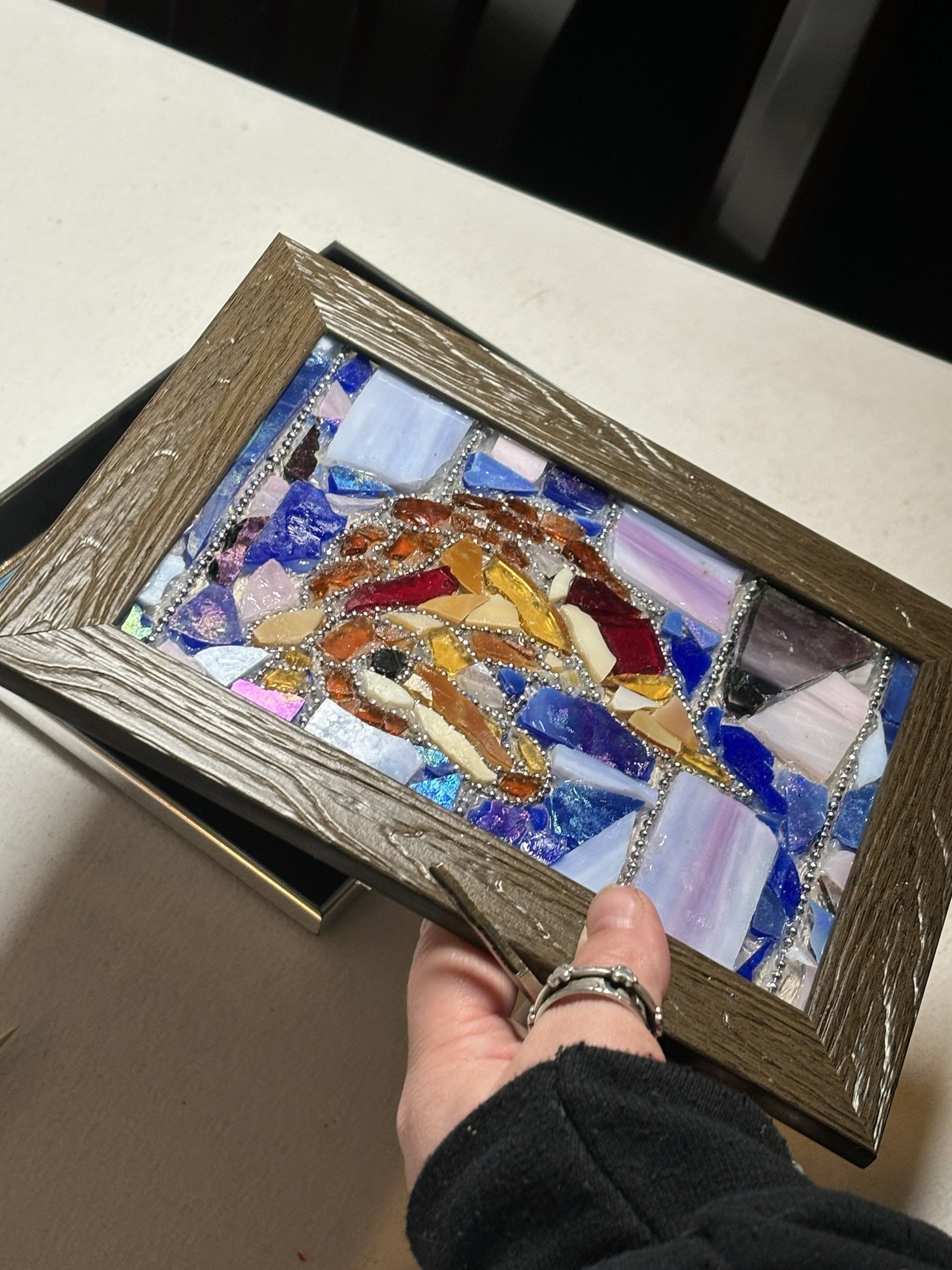 Hand holding a completed faux stained glass project in a wooden frame.
