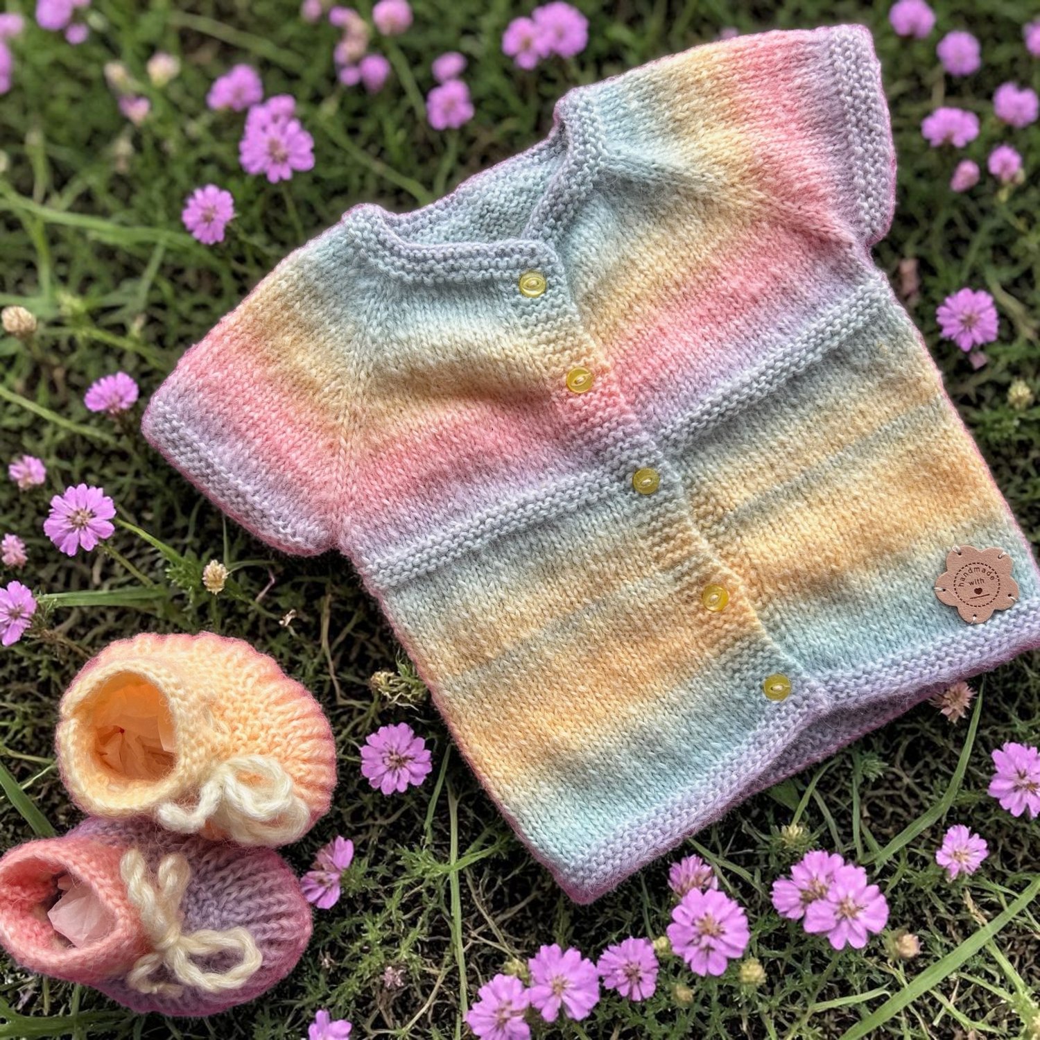 Hand-knitted rainbow blouse with pairing shoes on a grass and pink flowers background.