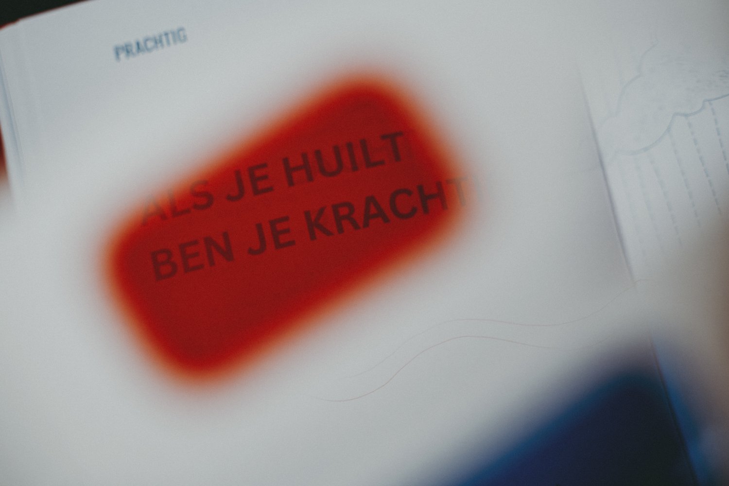 Close-up van een boekpagina gezien door een kartonnen kleurfilter-bril met rode lens. De tekst wordt deels bedekt en vervaagd door de bril.