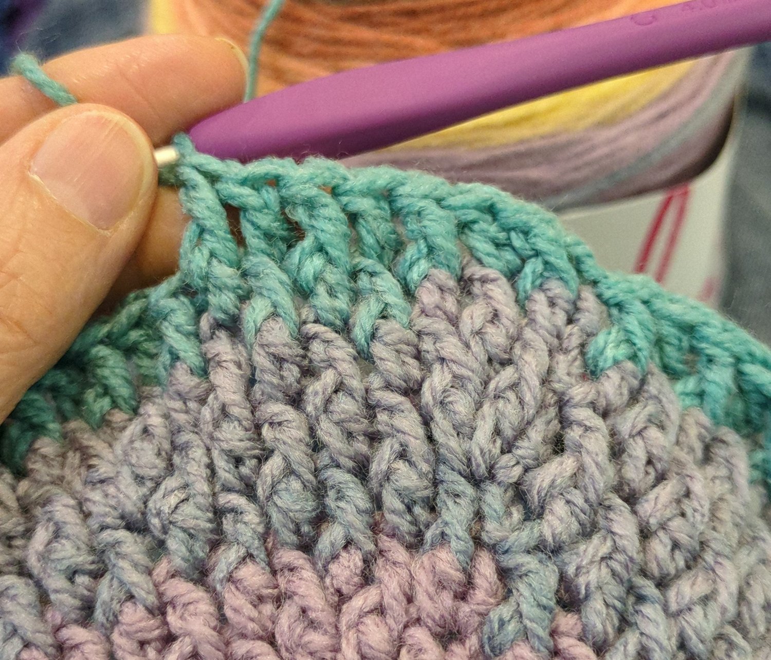 Close-up of textured crochet beanie crown in soft neutral yarn with overlay text reading “Pebble Ridge Beanie PDF Pattern” and a small illustrated cat logo in the corner.
