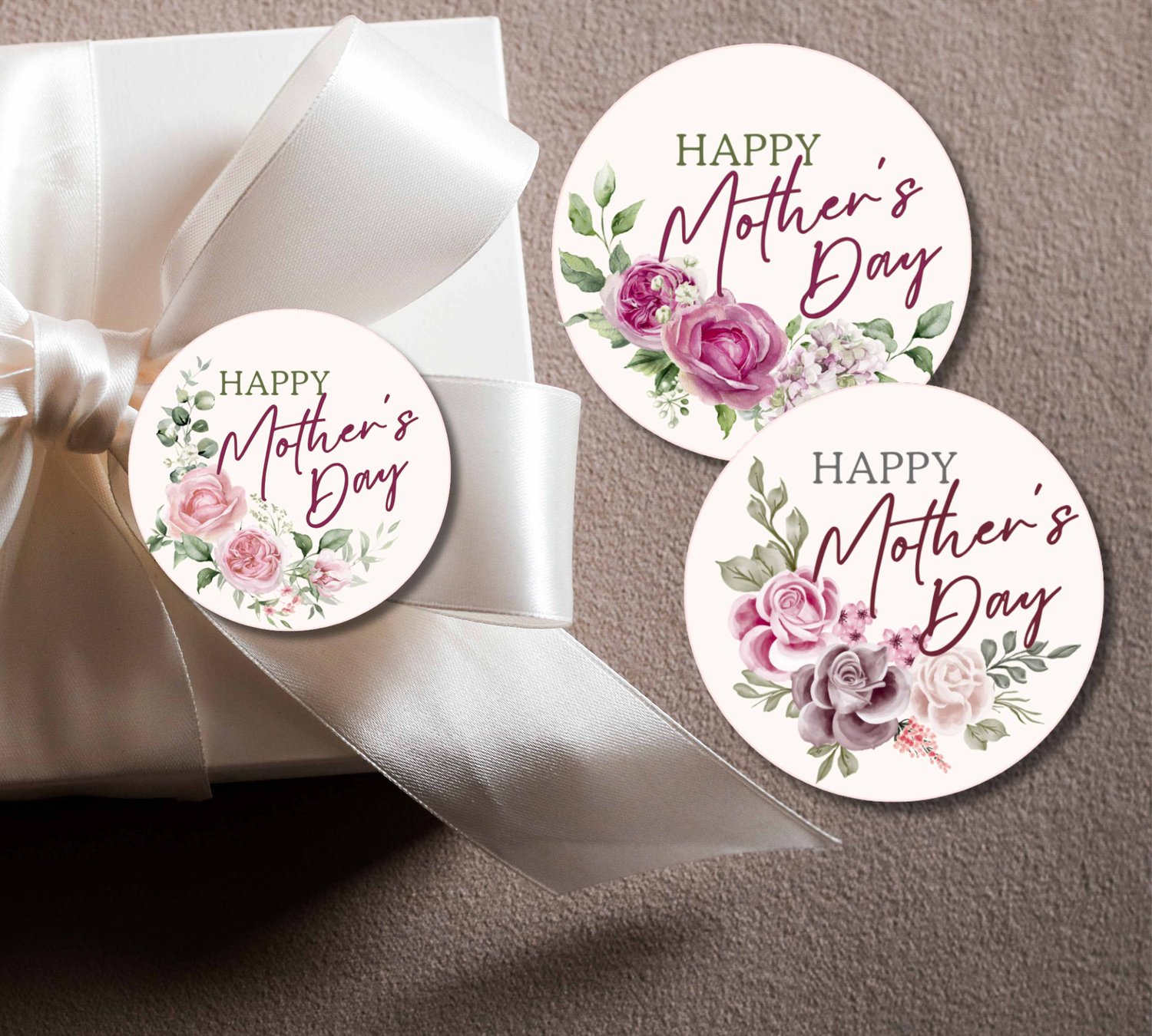 White gift box with satin bow, surrounded by three round floral “HAPPY Mother’s Day” tags in pink and green tones.