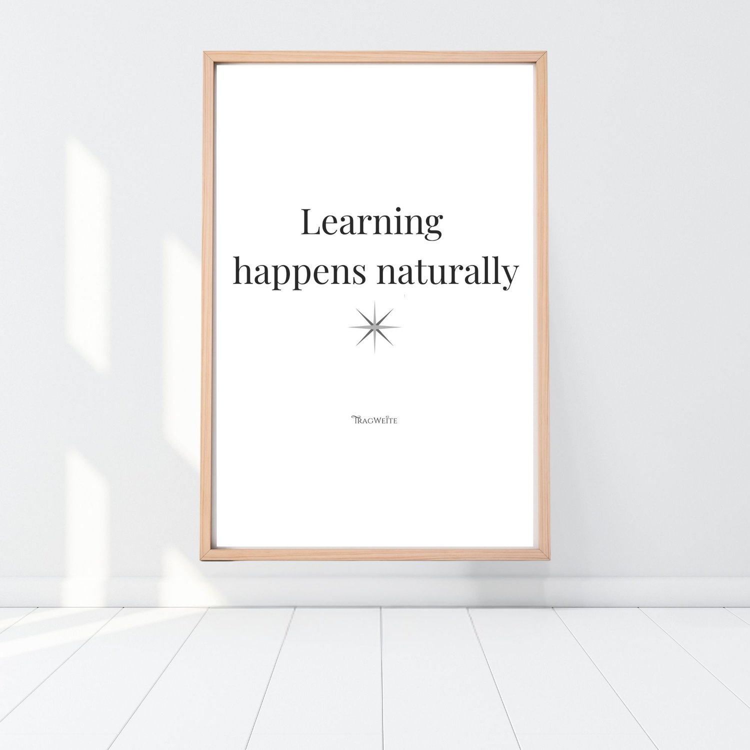 Framed printable poster "Learning happens naturally" in black and white, leaning against a white wall on a light wooden floor. Minimalist wall art by Tragweite. Gerahmtes Poster „Lernen geschieht natürlich" in Schwarz-Weiß, an eine weiße Wand gelehnt auf