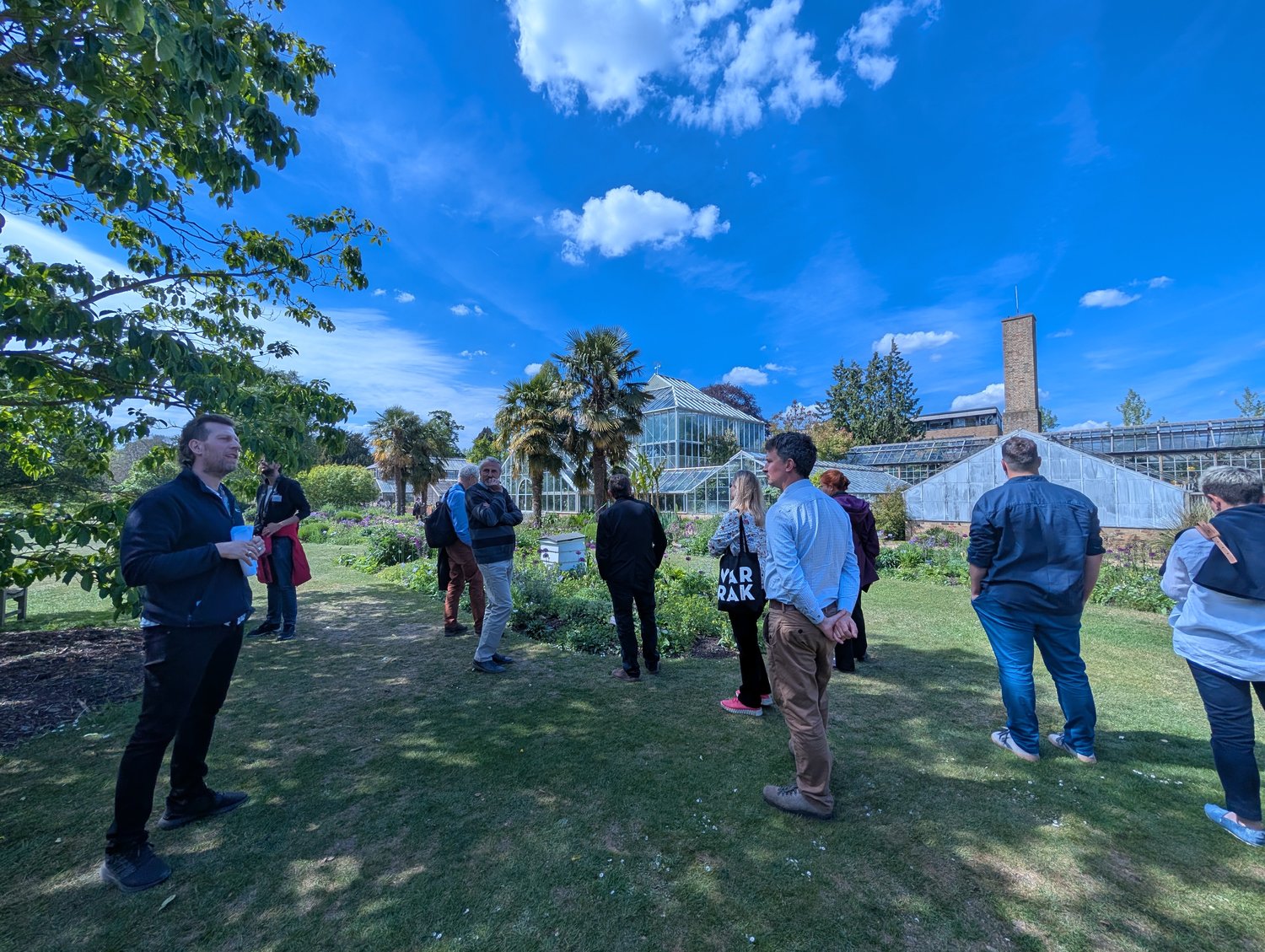 People gathered in the foreground, blue sky and glasshouse in the background