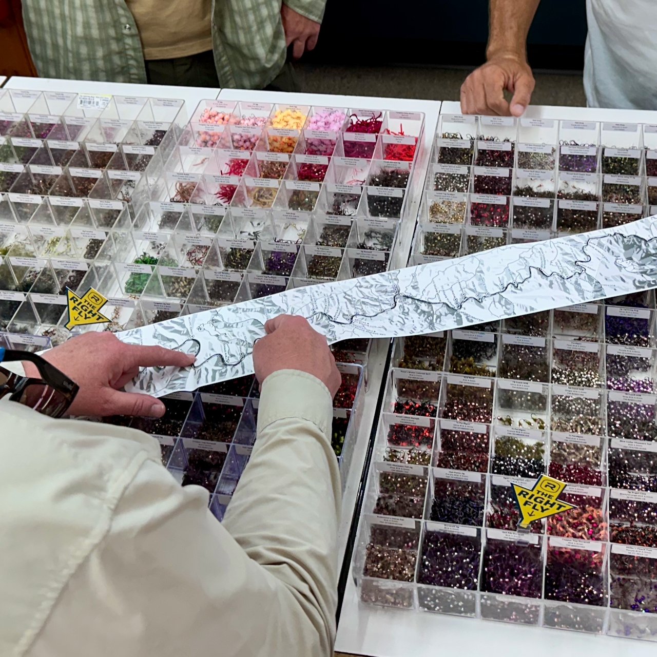 Lower Deschutes Ribbon Map unrolled across a fly bin at a fly shop, showing the full length of the map from bank to bank with several employees pointing out features