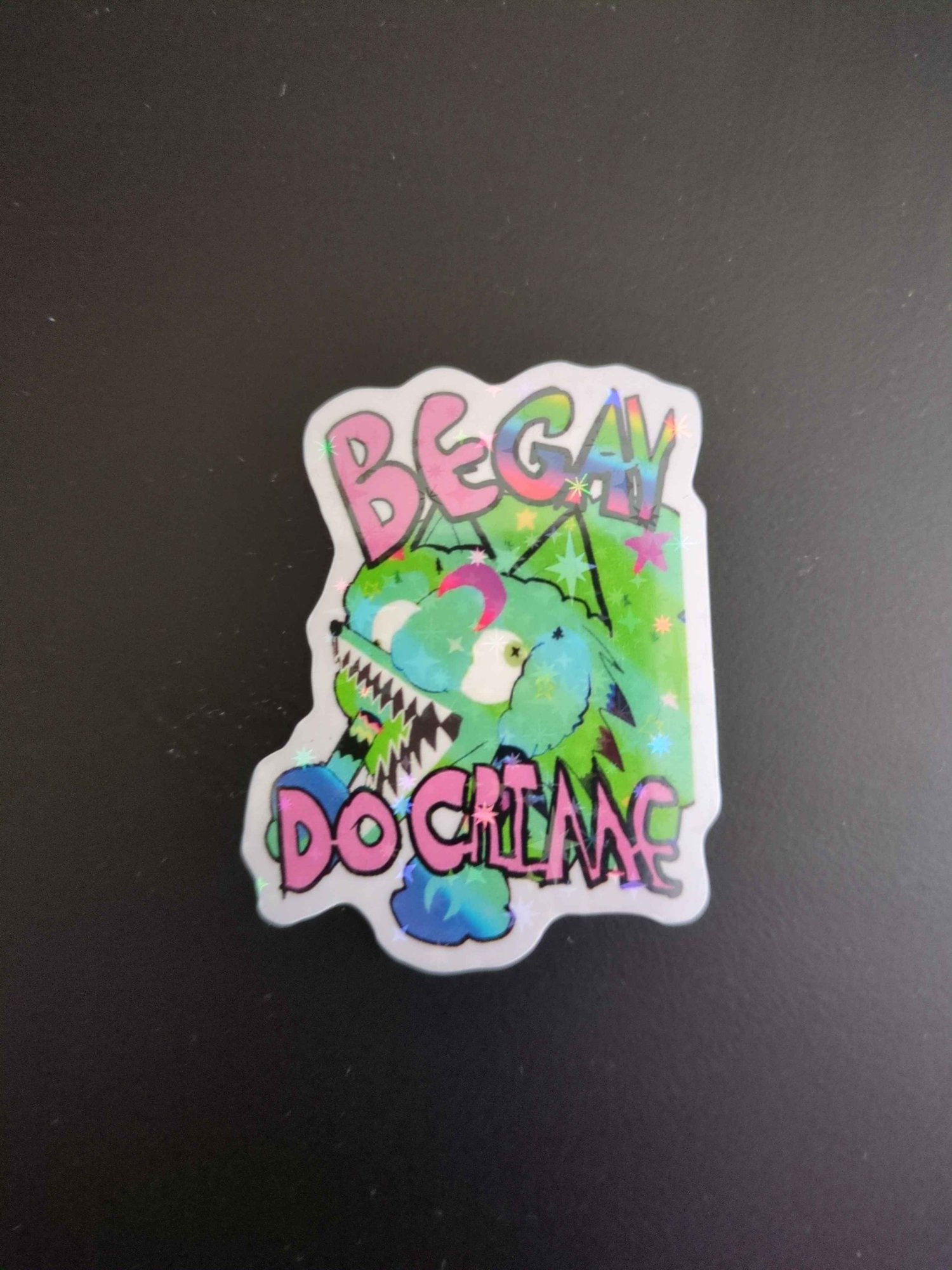 Green Sparkle COyote girl head in green sparkles covered in stars and moons blue green gradient with pink text that reads "Be Gay Do Grime" Gay text is rainbor. Wide mouth, braids and eyes looking the wrong directions.