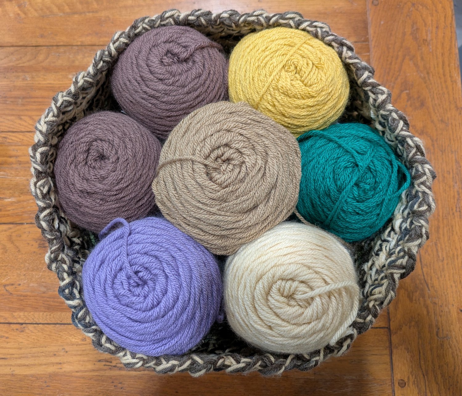 Assorted crochet yarn cakes in multiple colors inside a handmade crochet basket for a blog post about how to choose yarn for crochet projects, including yarn weight, fiber types, and beginner crochet tips.