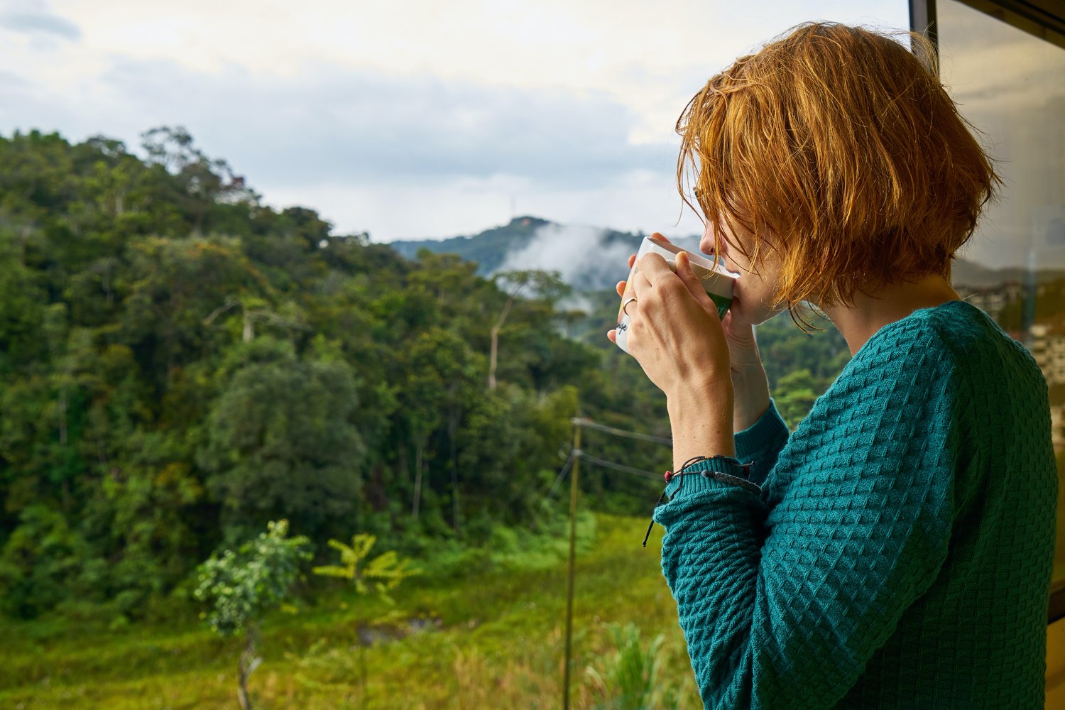 Woman sipping coffee while admiring nature from her porch. Demitasse Endeavors brewing mindful moments through curated morning ritual kits and gifts. Specialty coffee kit. Self-care morning gift.