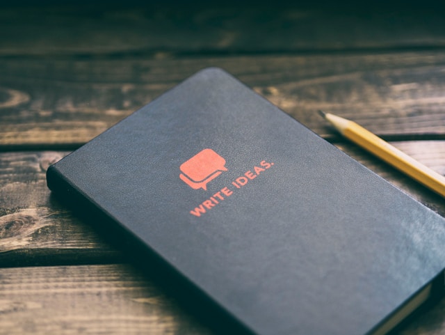 A notebook with the words 'Write Ideas' on the front by Photo by Aaron Burden from Unsplash
