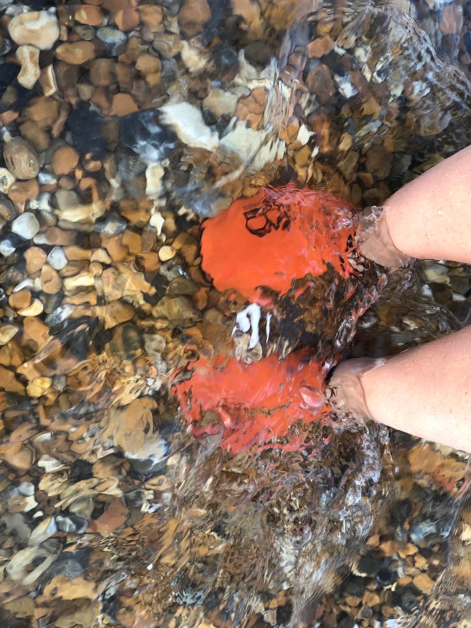 Orange water shoes on a person's feet in clear water