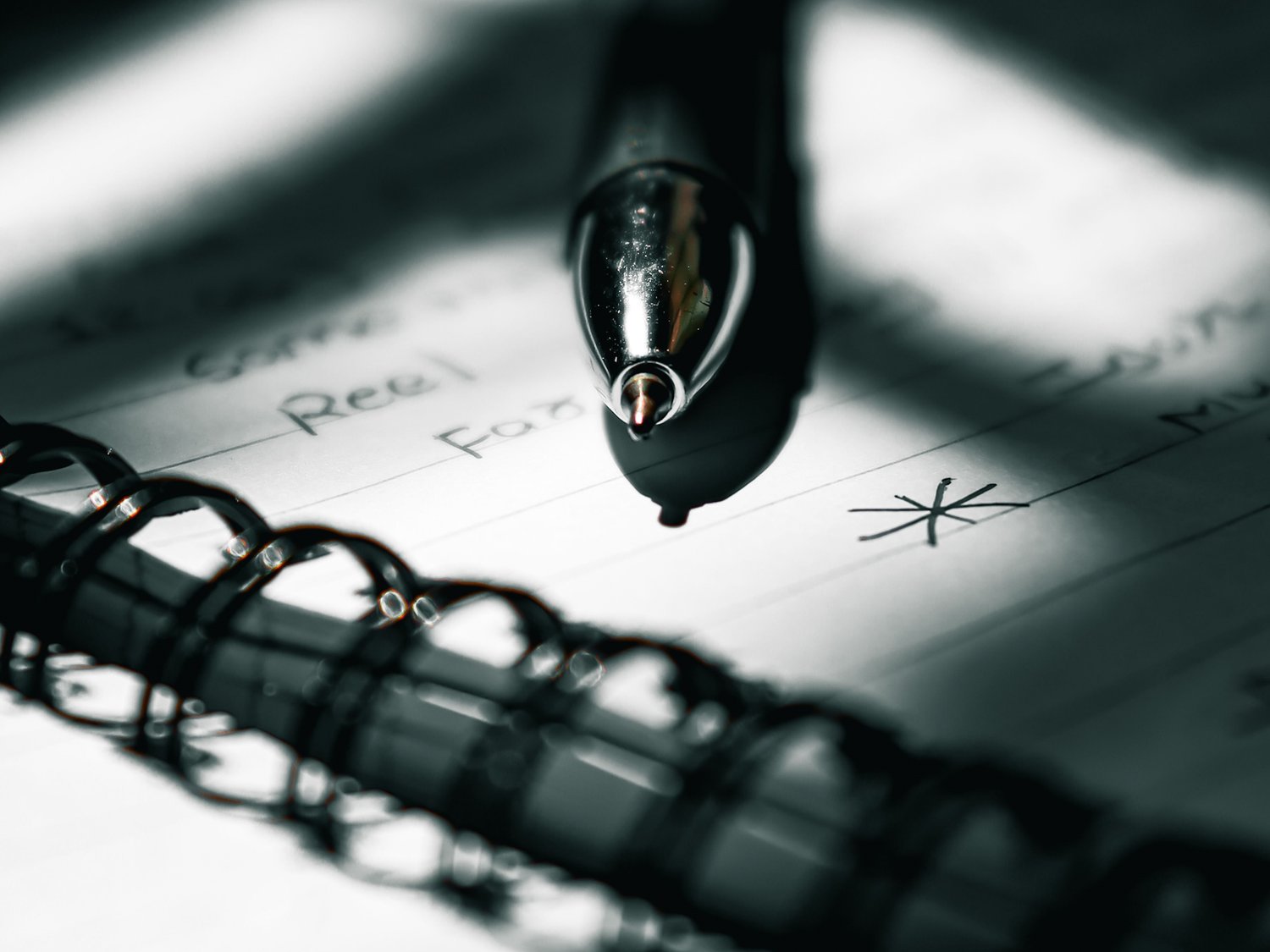 Close-up of a pen resting on a spiral notebook with shadows. Minimalistic and artistic composition.