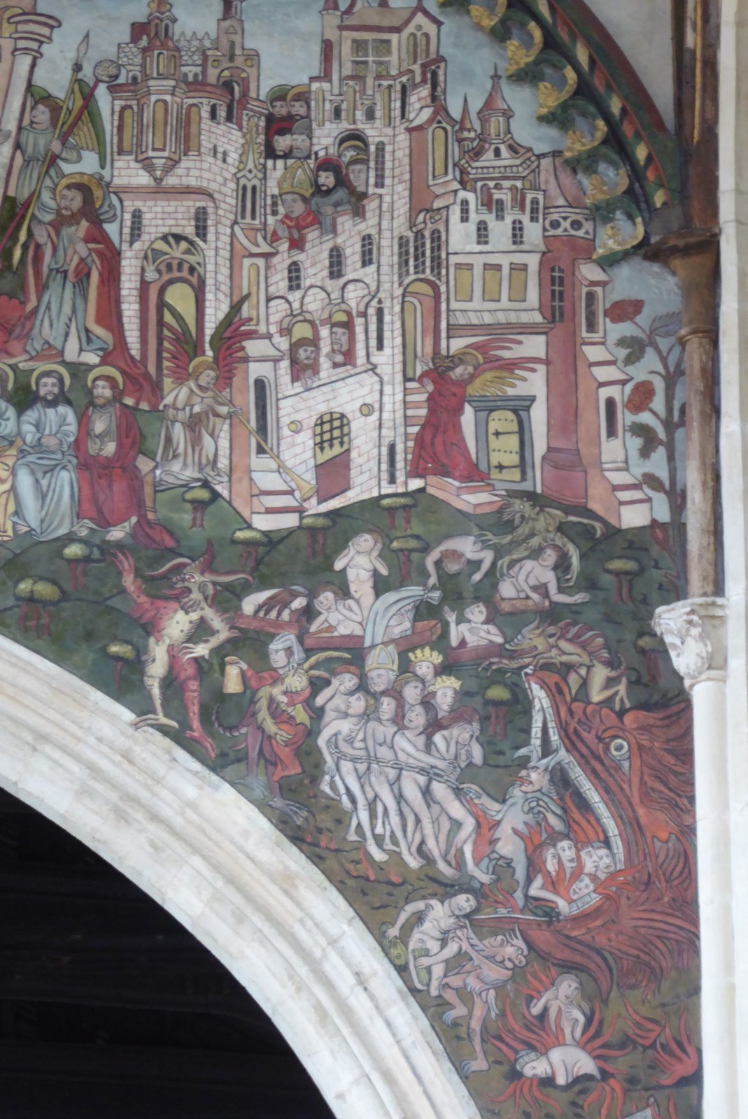 The right hand side of a chancel arch painted with a doom painting. There is a city at the top and beneath a fish-like jaws of hell with people being pulled out of it.