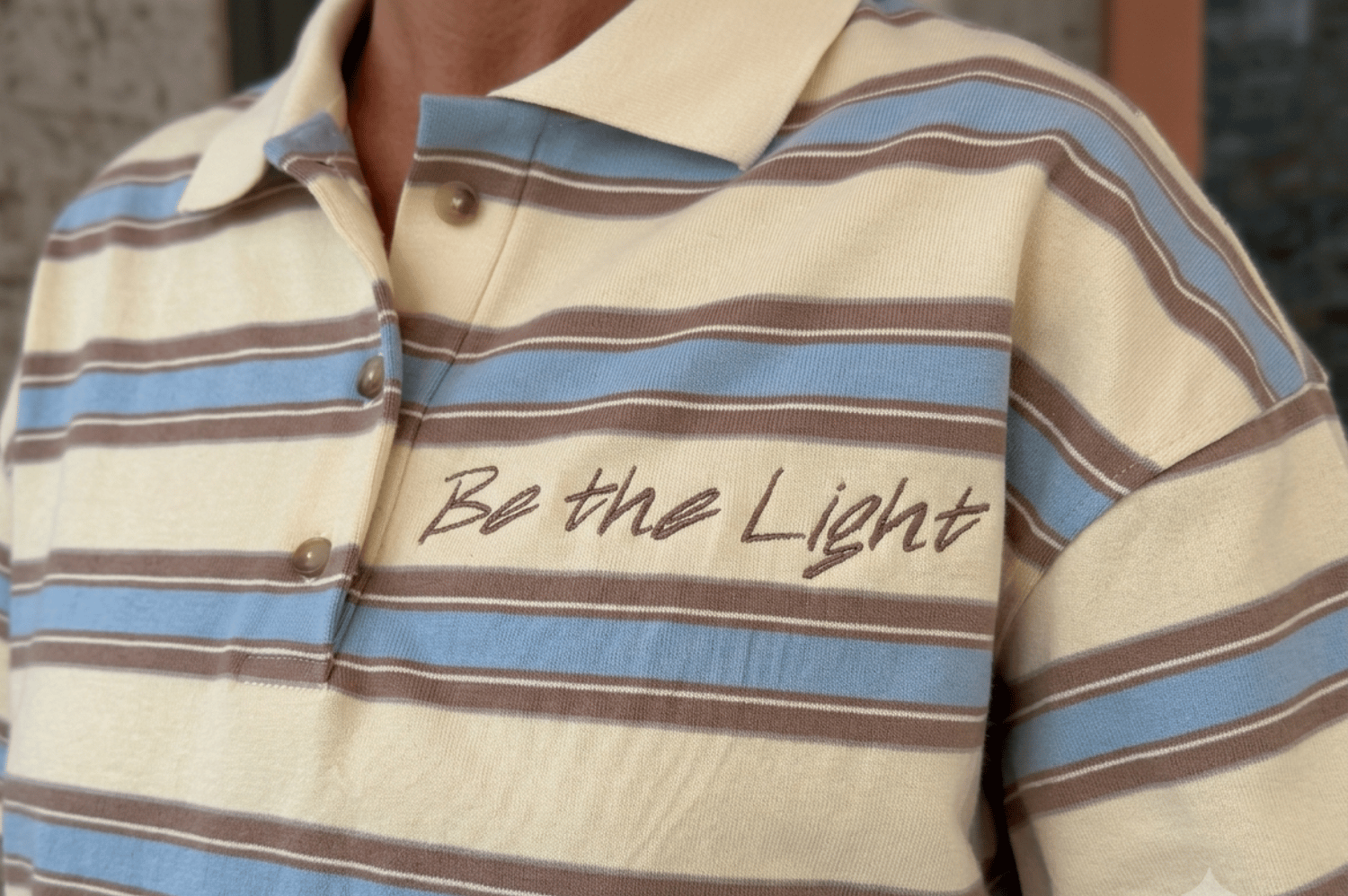 Striped polo shirt featuring a button placket and embroidered Be the Light typography by Firstype
