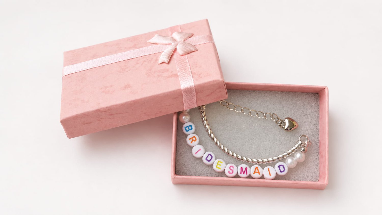 Handmade bridesmaid proposal charm bracelet featuring a silver twisted wire bangle, white pearls, rainbow BRIDESMAID letter beads, and a dangling silver heart charm. in luxury pink box