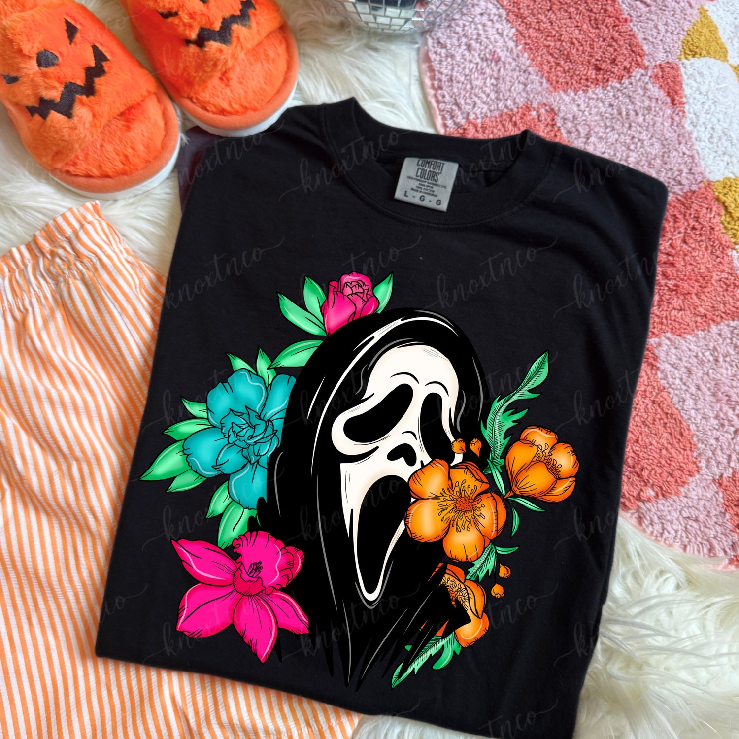 Ghostface floral Halloween graphic on a black Comfort Colors t-shirt featuring bright pink, turquoise and orange flowers, spooky season horror tee.