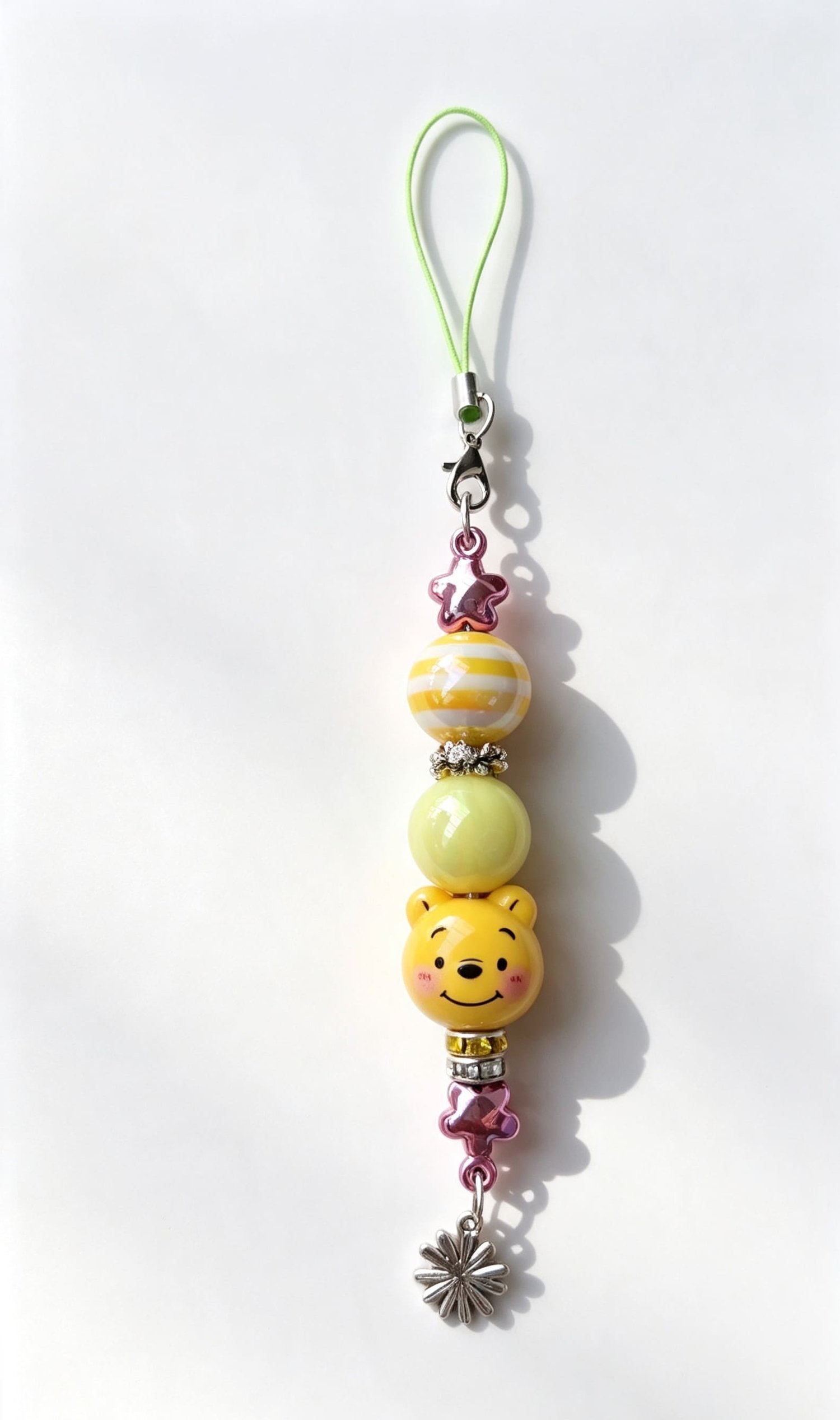 Close-up layout of a custom yellow bear phone charm by Sparkling Resin Delights, featuring a smiling cartoon bear silicone focal bead, pastel yellow and striped accent beads, crystal rhinestone spacers, metallic pink star beads, and a silver flower charm