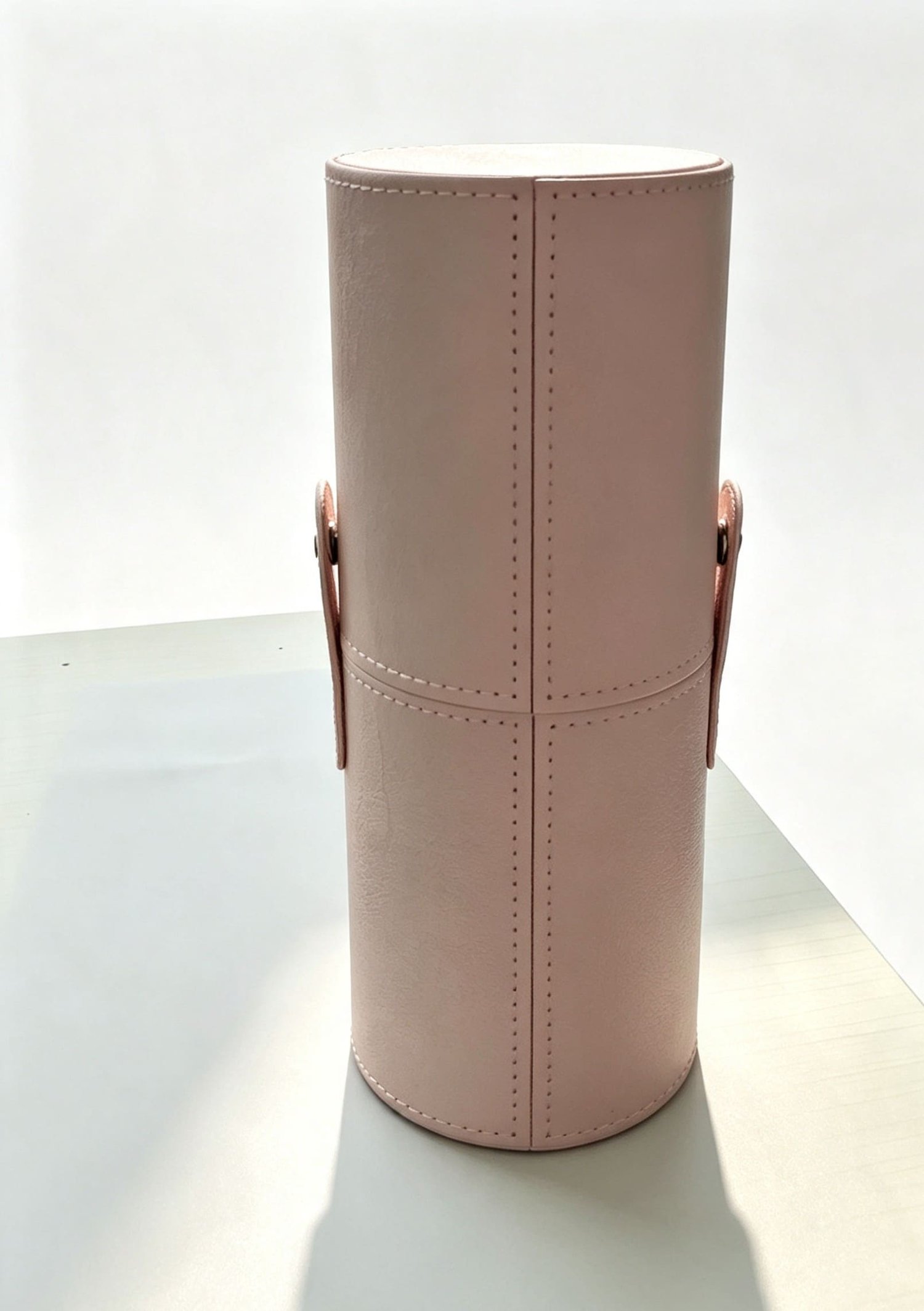 Closed pink faux leather cylinder makeup brush travel case with decorative vertical stitching and side snap fasteners.