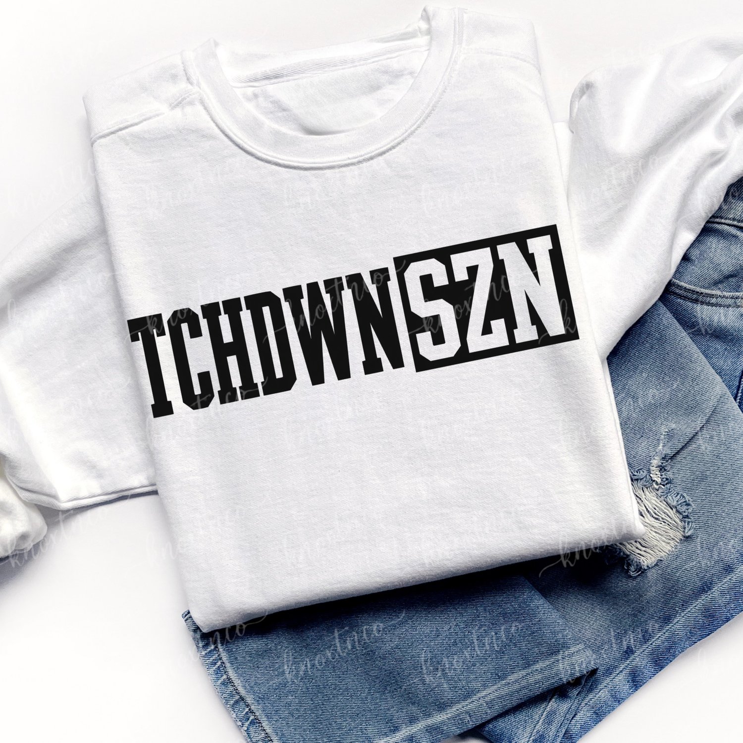 White T-shirt sweatshirt featuring a bold white varsity-style “TCHDWN SZN” graphic across the front, shown folded on top of blue denim jeans.  Touchdown season sweatshirt unisex size small to 3X