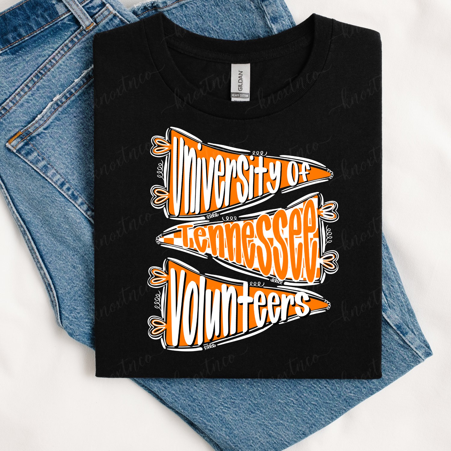 Black Gildan T-shirt featuring an orange and white University of Tennessee Volunteers pennant graphic, styled with three stacked vintage-inspired pennants and bold lettering, displayed on blue denim.
