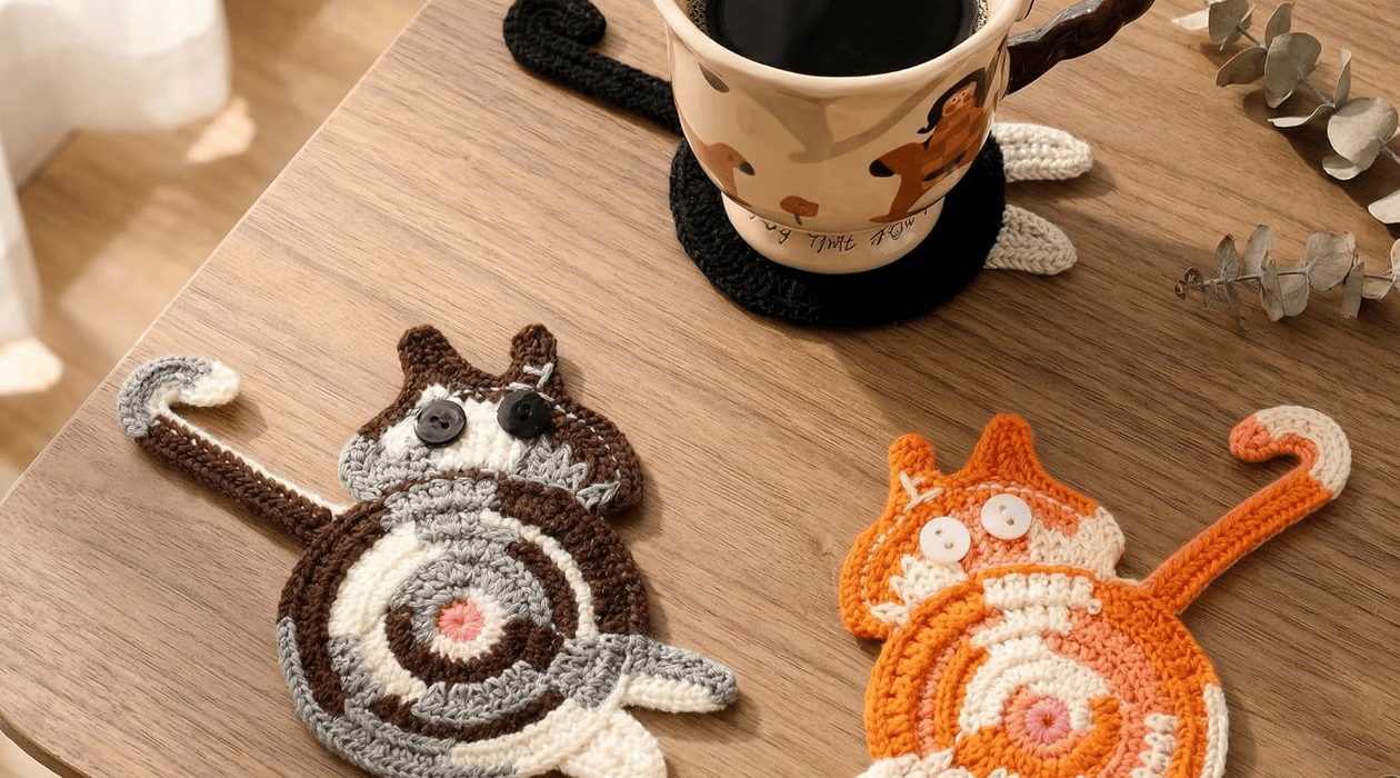 Handmade cat-shaped coasters displayed on a wooden table with a coffee mug