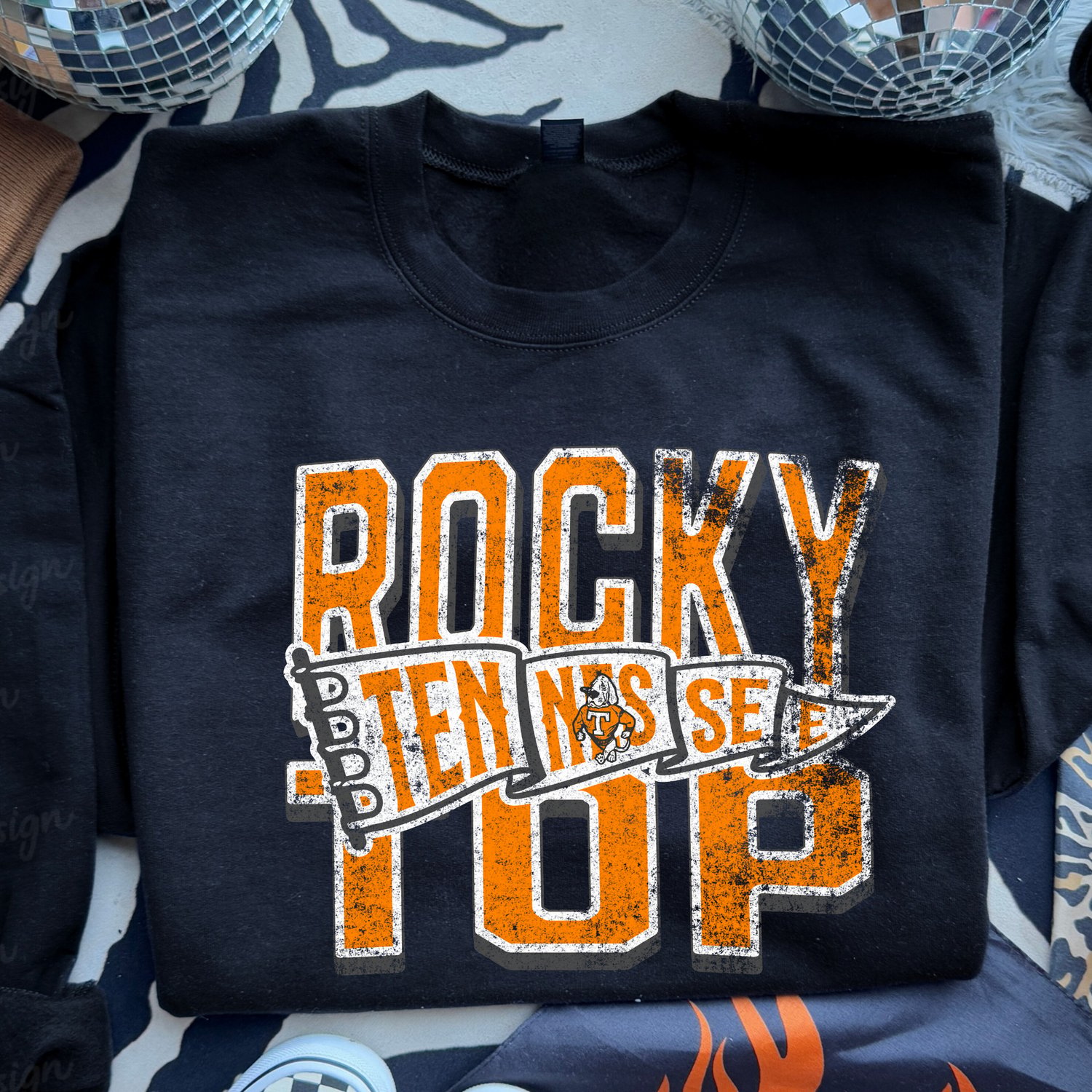 Black Gildan T-shirt featuring a distressed orange, white, and gray “Rocky Top Tennessee” graphic with a Smokey dog illustration, displayed on folded blue jeans.
