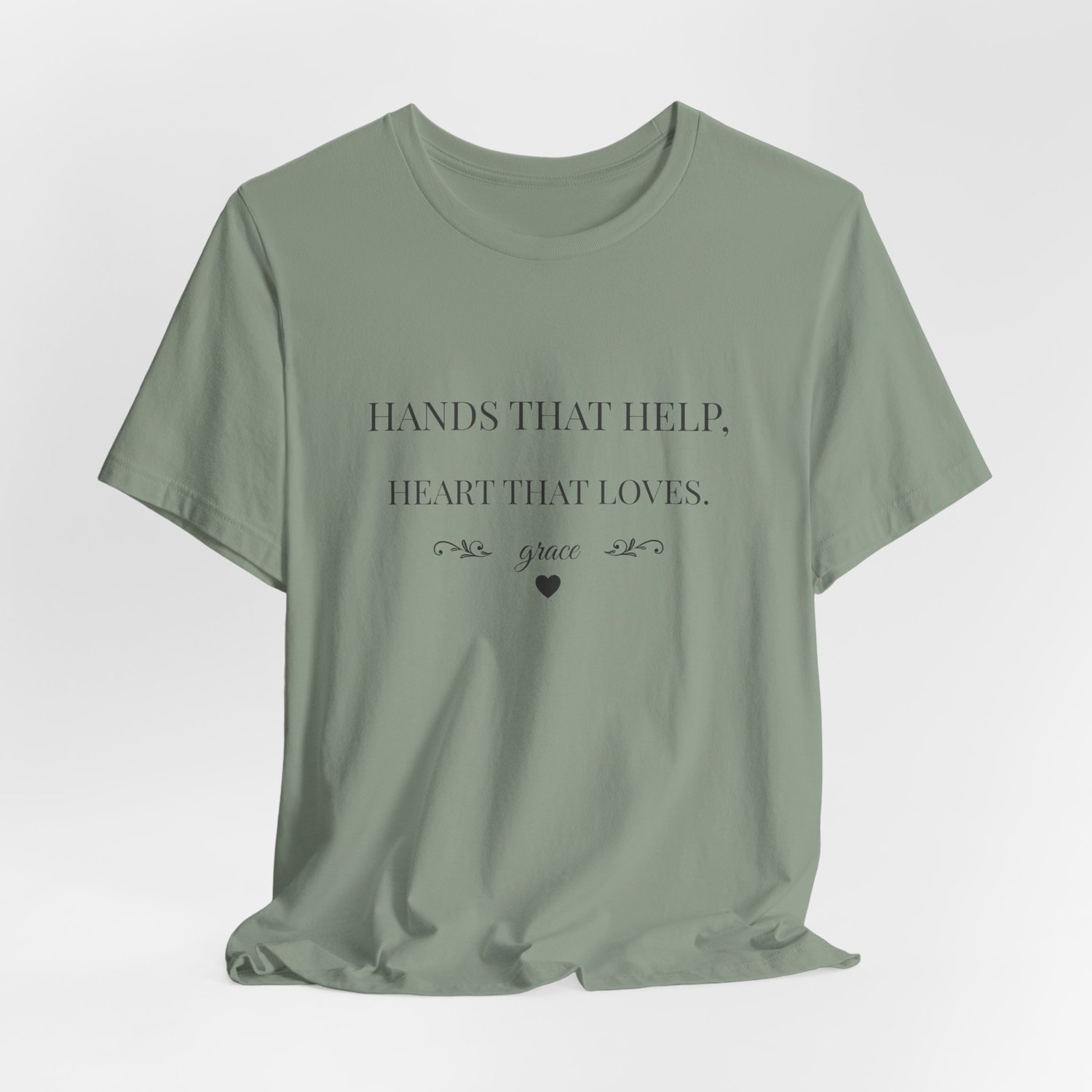 Hands That Help Heart That Loves caregiver shirt wrinkled flat lay in Sage.