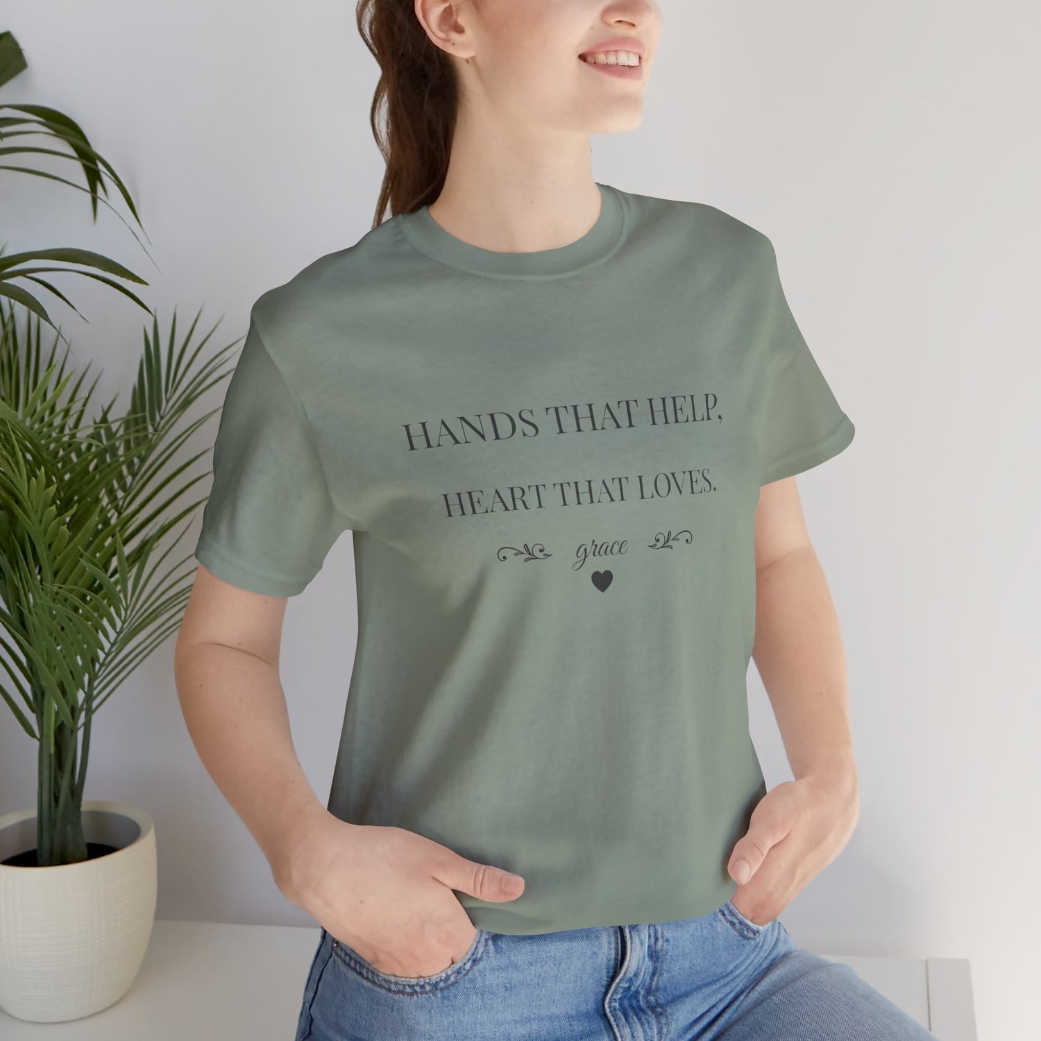 Caregiver shirt Hands That Help Heart That Loves modeled sitting in Sage.