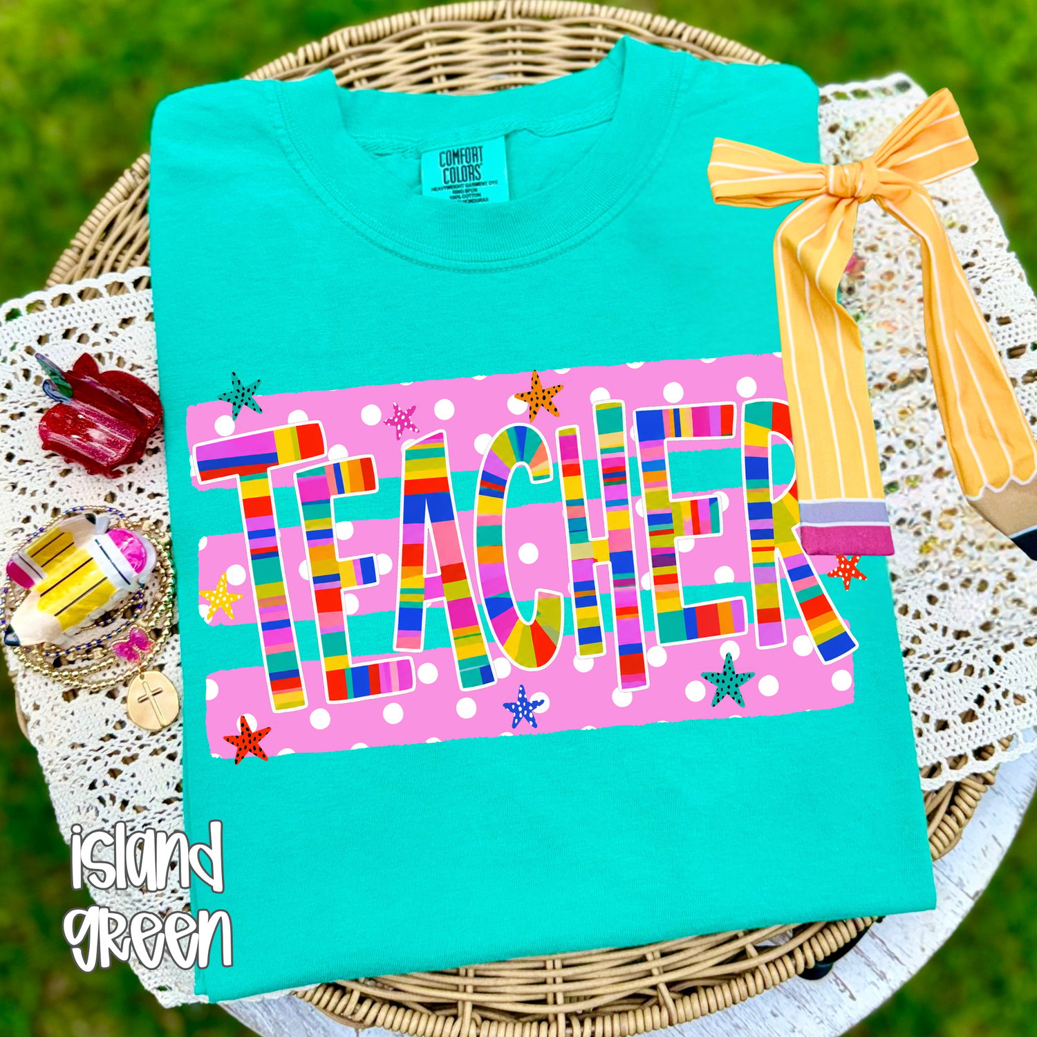 Comfort Colors t-shirt featuring a bright colorful “TEACHER” design with pink polka dot background, star accents, and pencil graphic.
