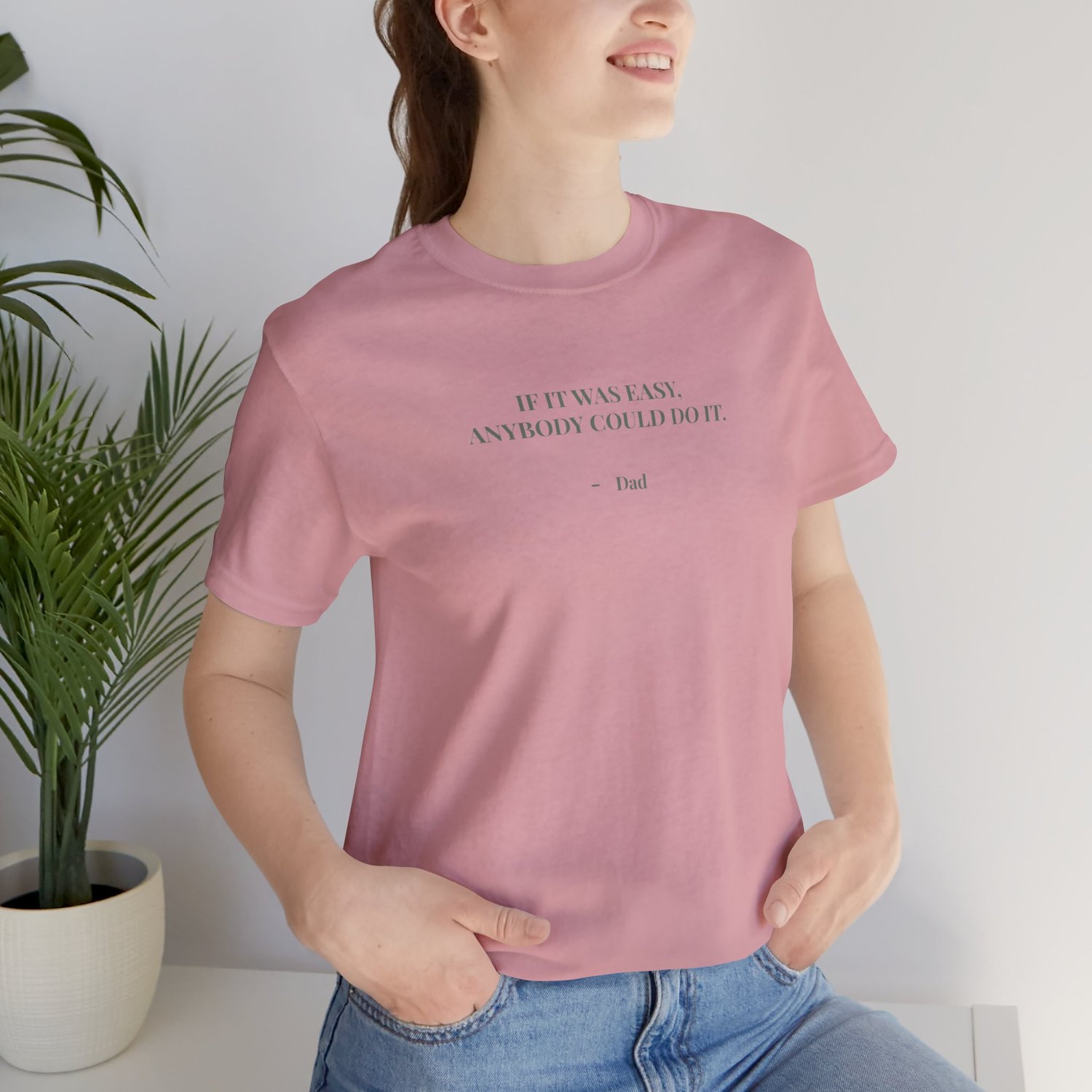Woman wearing a orchid t‑shirt with the quote ‘If it was easy, anybody could do it. — Dad’ while sitting indoors.