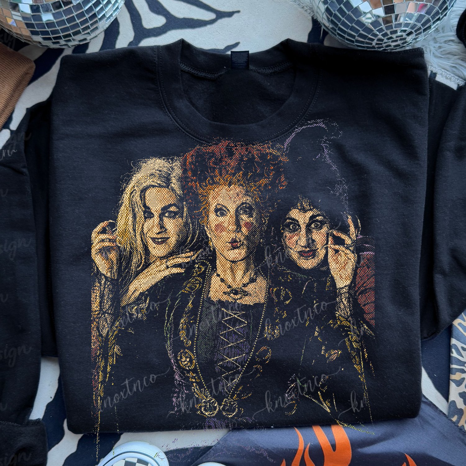 "Black apparel featuring a vintage tapestry-style graphic print of the three Sanderson Sisters witch from Hocus Pocus for Halloween.