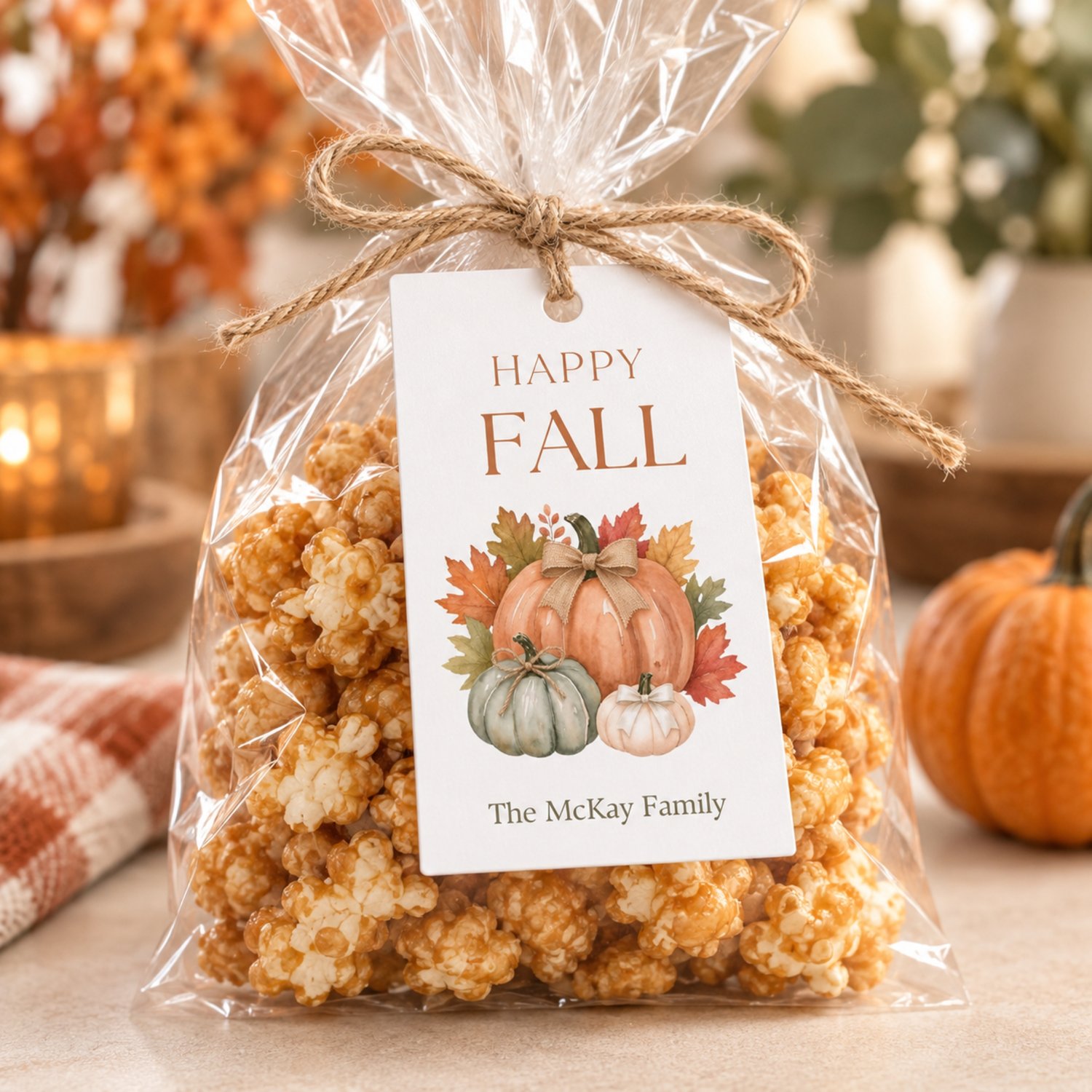 A rectangular white gift tag temaplate featuring the text HAPPY FALL in brown letters at the top and editable text at the bottom. The center displays a watercolor illustration of three pumpkins in orange, green, and white with autumn leaves.