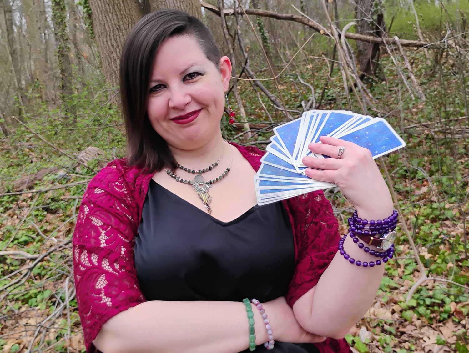 Photograph of Evylyn Rose looking toward the direction of the camera, holding up a fanned out stack of Tarot cards. Photograph by Ryan Hobbs, 2025