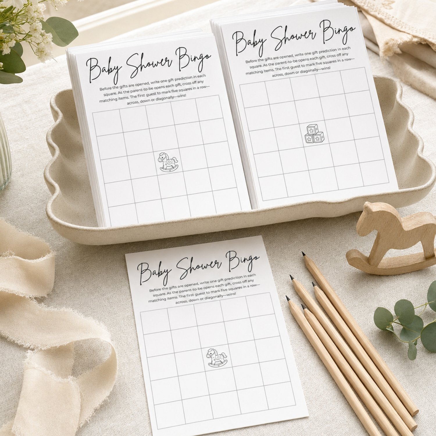 Two printable black-and-white Baby Shower Bingo cards featuring 5-by-5 blank grids, game instructions, and center free-space illustrations of a rocking horse and toy blocks.