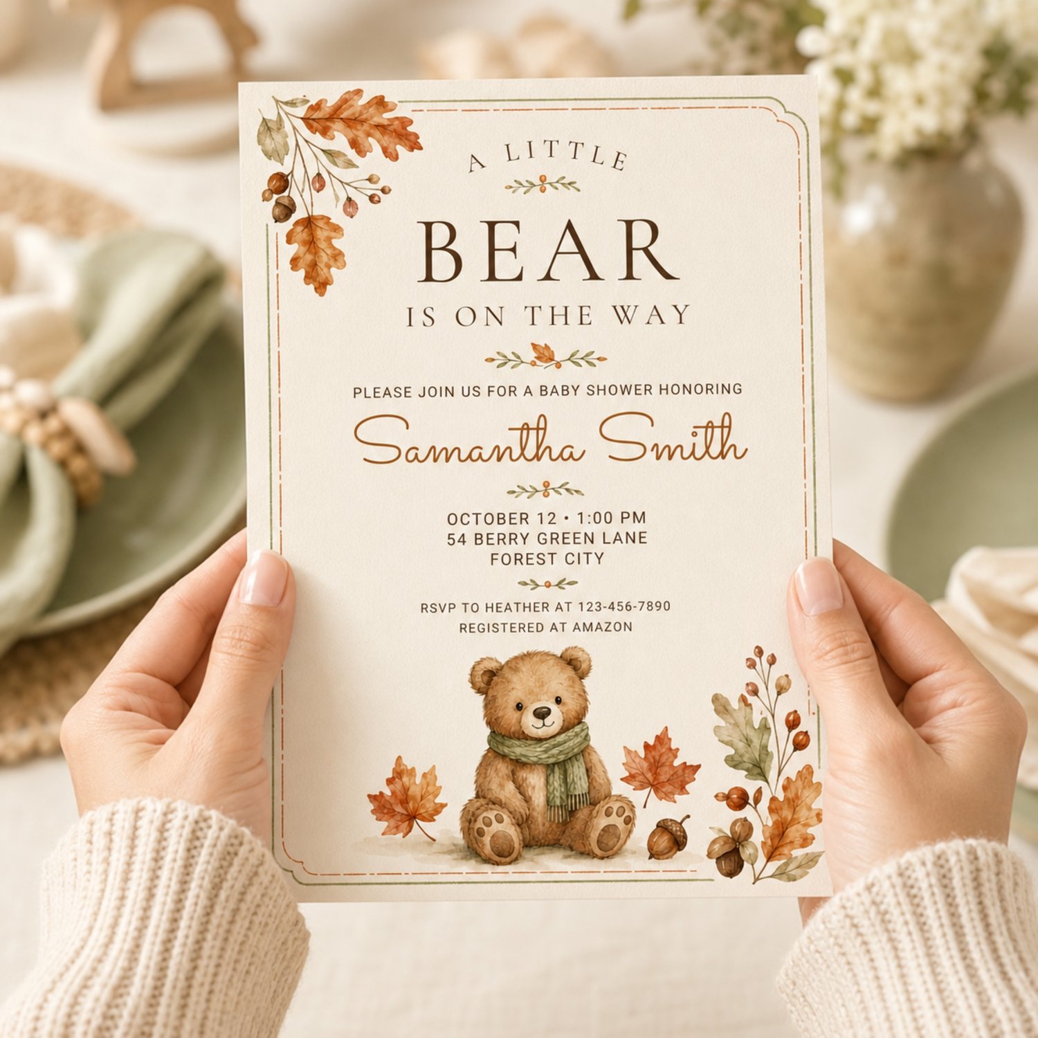 Editable 5 by 7 fall baby shower invitation featuring a watercolor teddy bear in a green scarf, autumn leaves and acorns with “A Little Bear Is on the Way” wording.