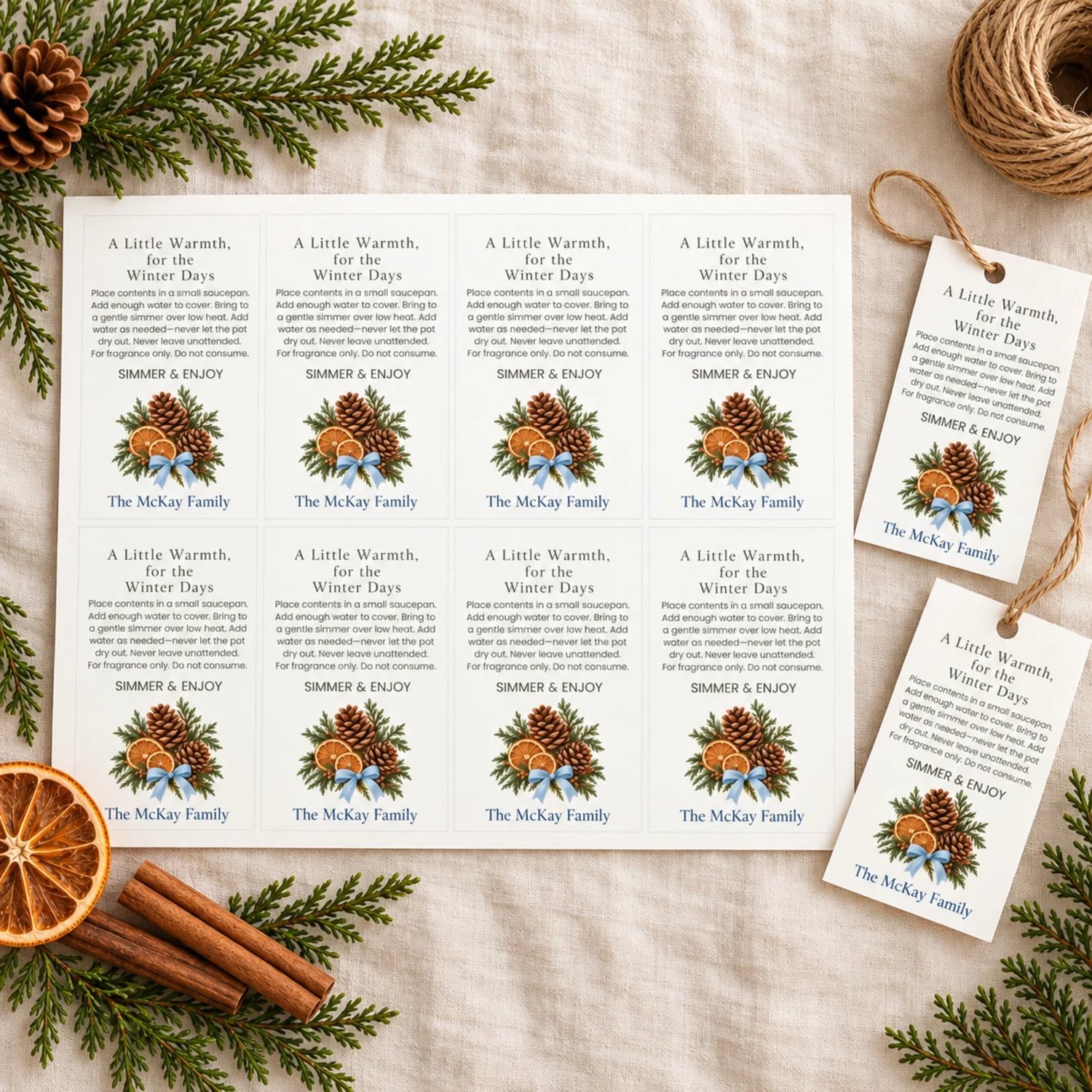 Landscape printable sheet of eight rectangular winter simmer pot gift tags with olive text, pinecones, dried orange slices, evergreen foliage and blue bows. Each includes simmering directions and a personalized family name.
