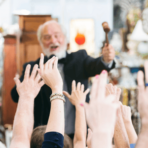 auctioneer with raised gavel in front of raised hands bidding on item up at auction