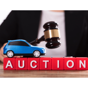 "auction" is spelled out in white letters on red blocks with blue car and gavel with auctioneer in background wearing a white shirt and black suit jacket