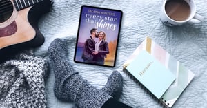 A tablet with the sweet romance cover for Every Star that Shines lays on a bed near crossed feet, a dream journal, a guitar, and a mug of coffee.