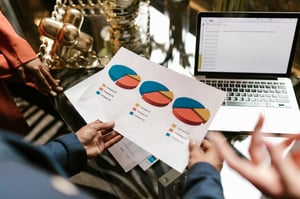 sheet of paper with three pie charts, a laptop, and multiple hands